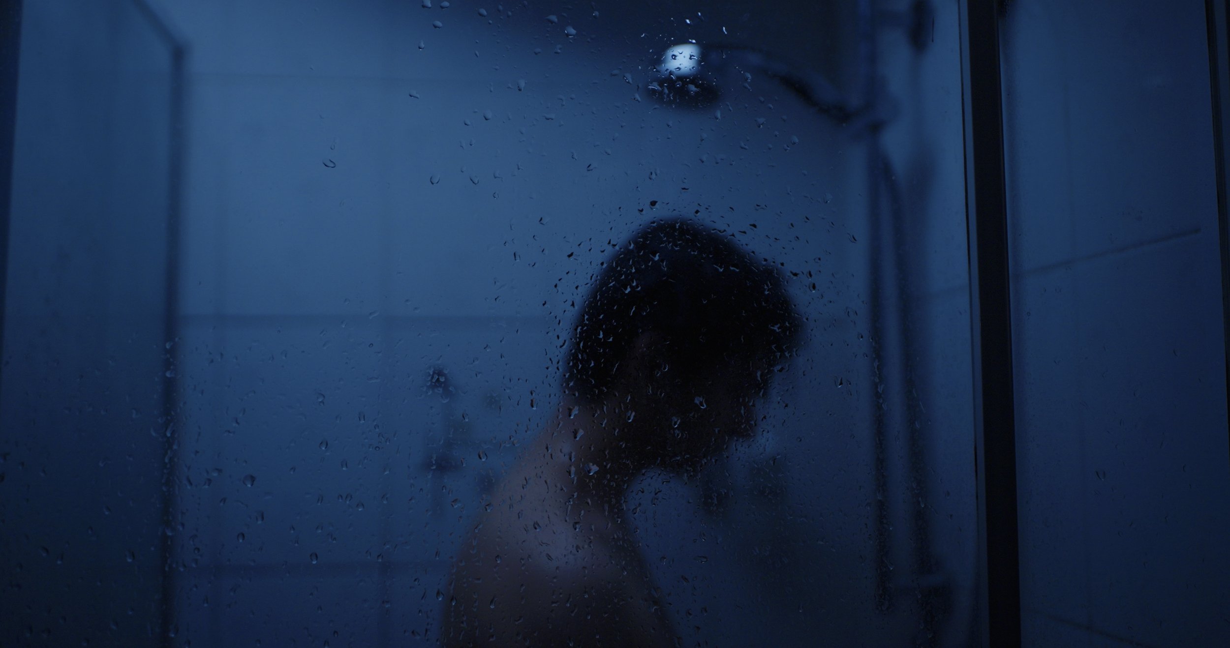 Blurred person seen through a blue-tinted, water-covered glass shower door