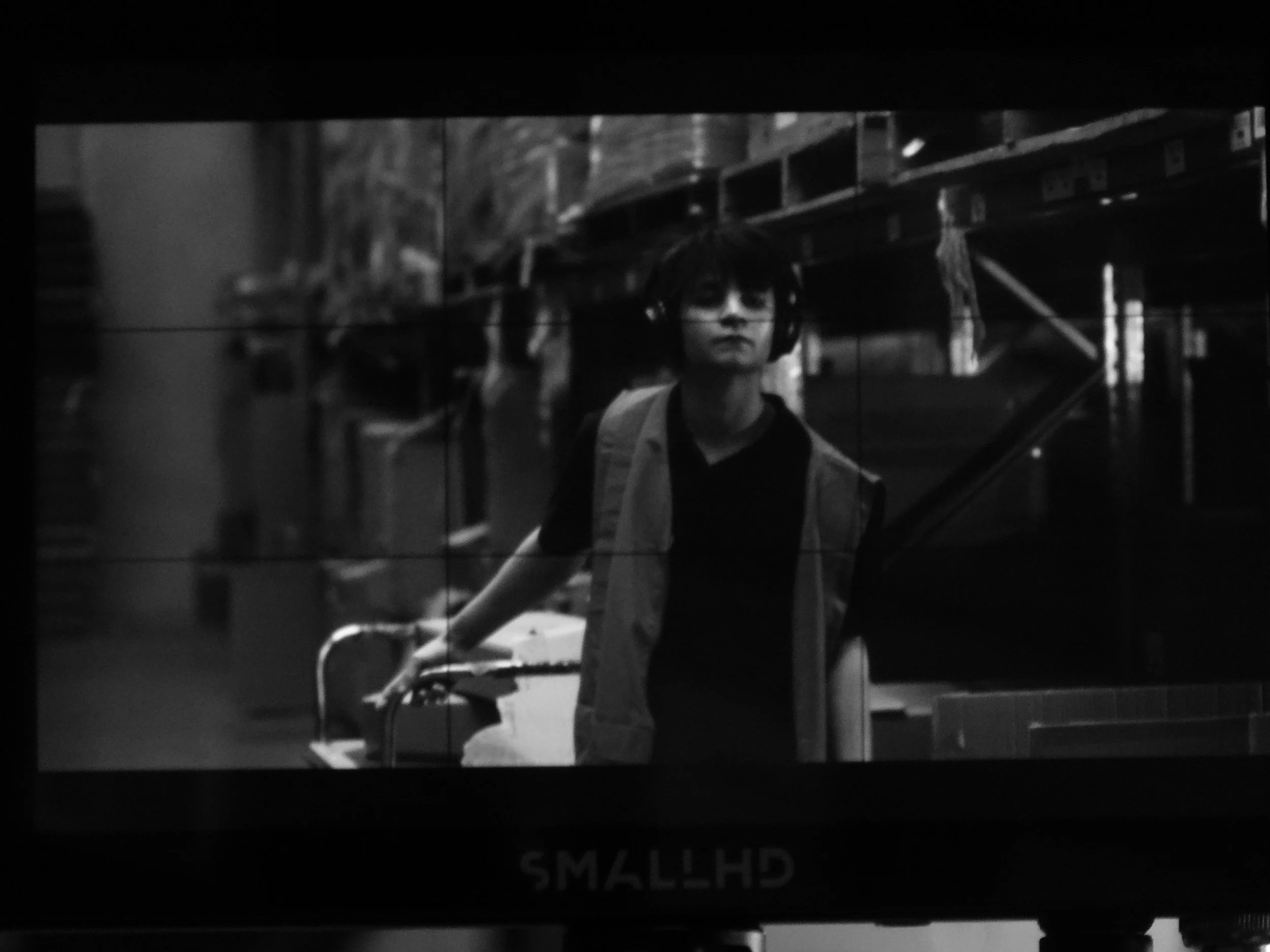 Black-and-white image of a person wearing headphones and standing beside audio equipment in a recording studio.