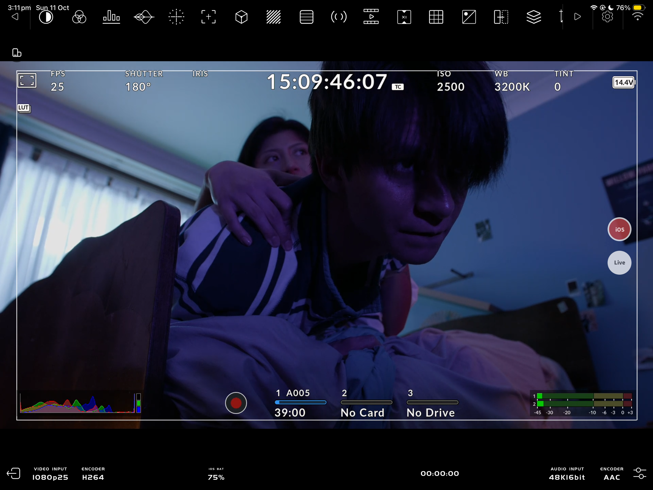 Camera monitor showing a blue-lit scene of a distressed person leaning forward while another person holds their shoulder.