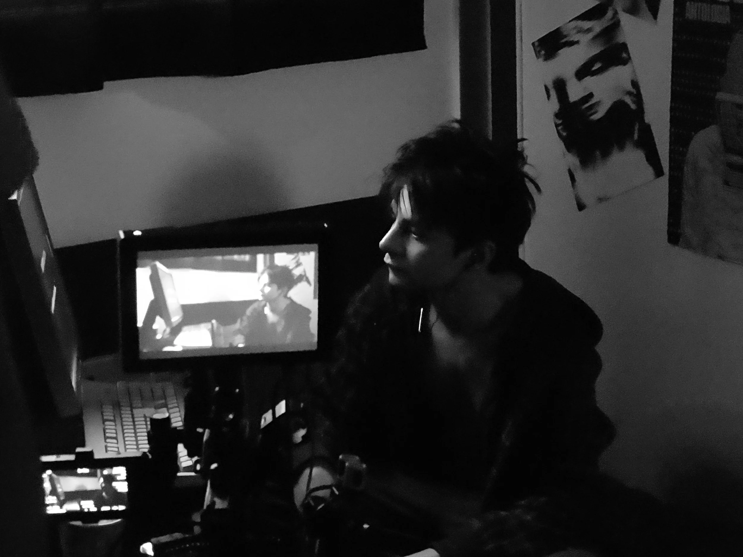 Black-and-white photo of a person seated at a computer in a dimly lit room, with an image displayed on the monitor.