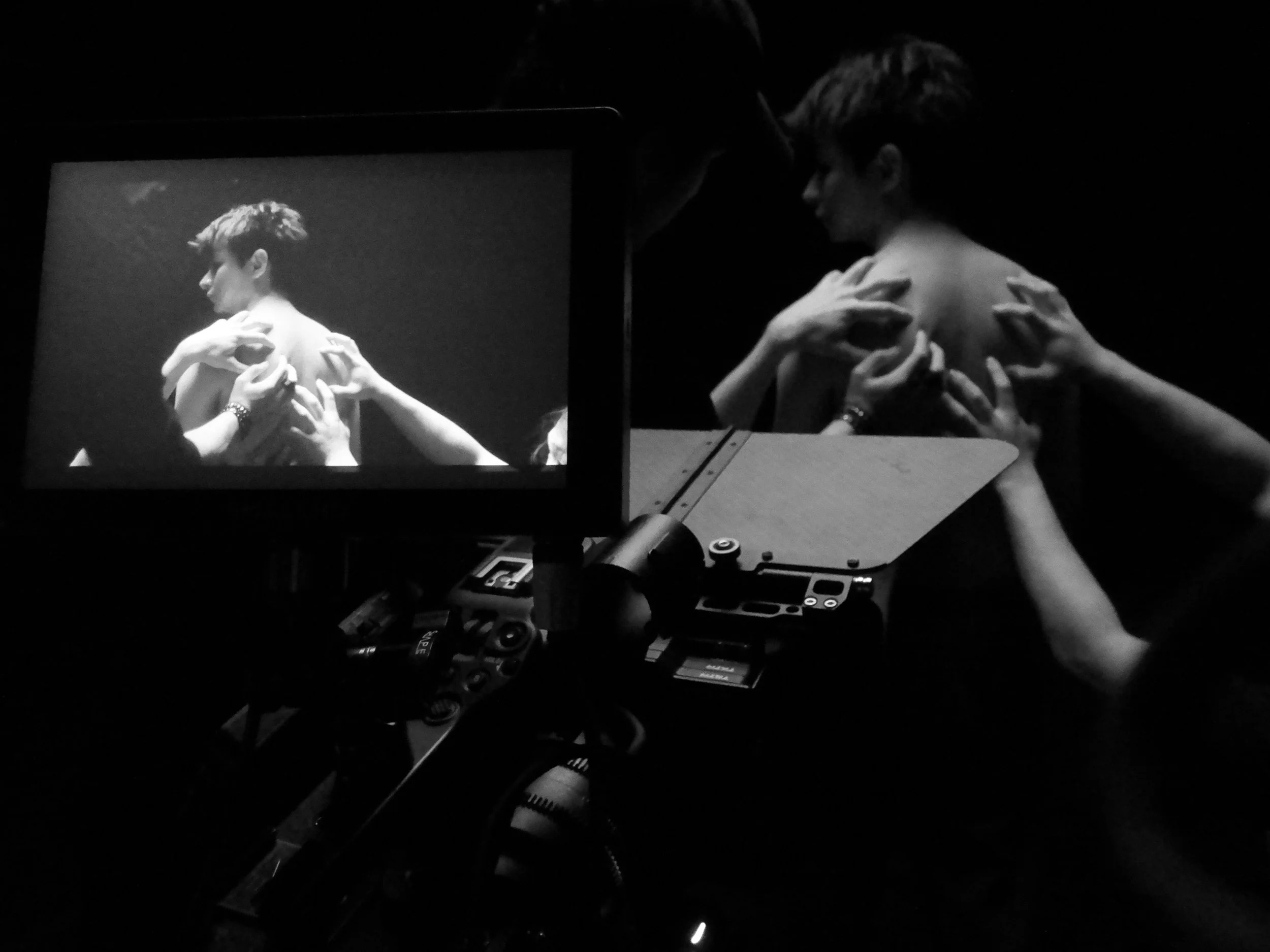 Black and white photo of a person receiving a shoulder massage, with the image viewed on a camera screen showing the scene.