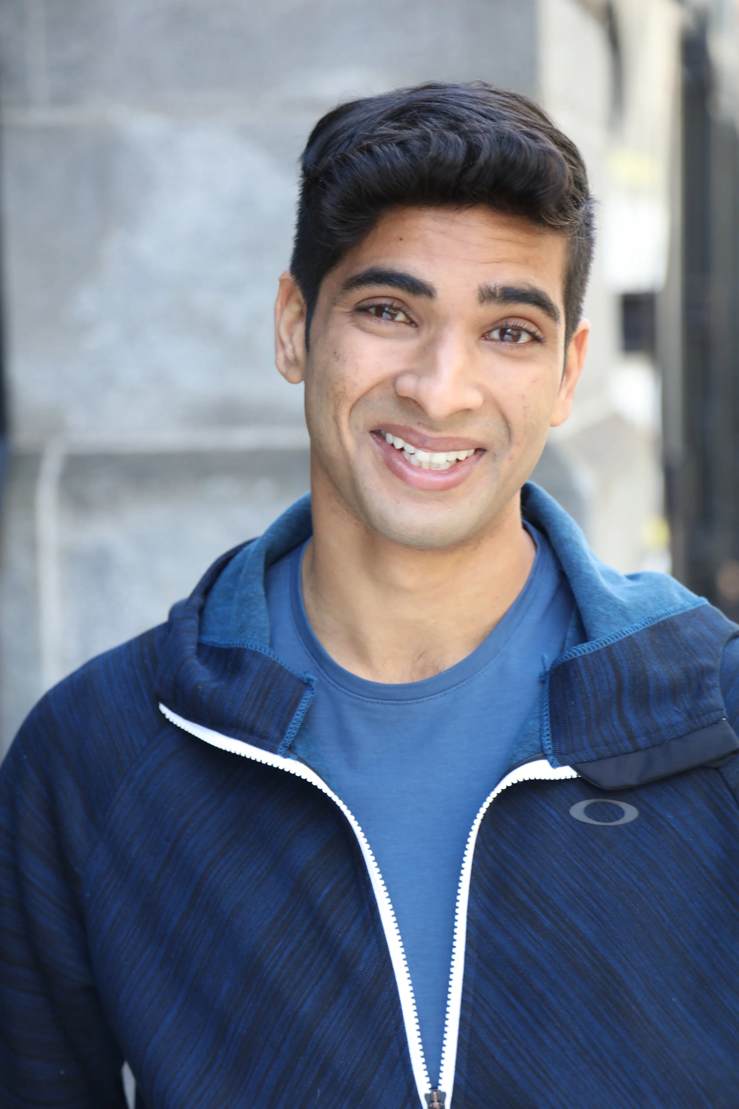 Smiling young man in a blue shirt and zip-up jacket, close-up portrait indoors
