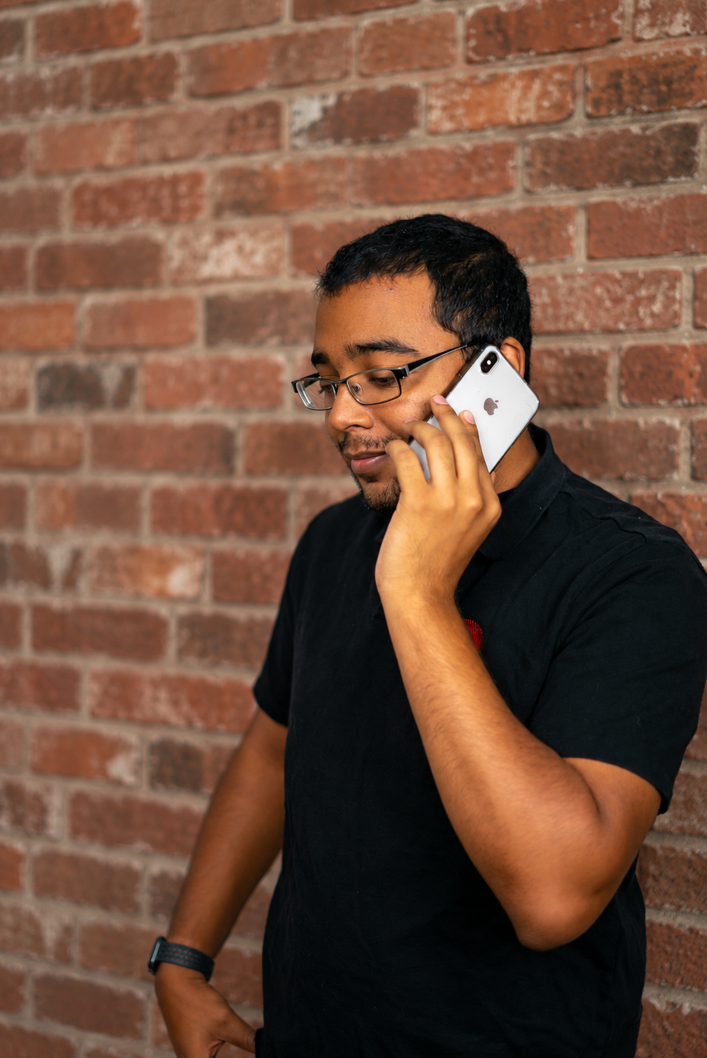 Paul Alleyne on a phone call in front of a classic brick wall.