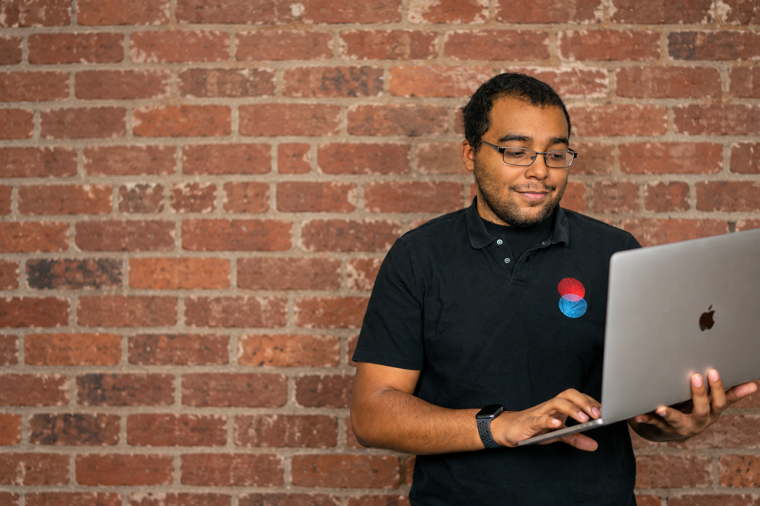 Paul Alleyne working on a laptop in front of a classic brick wall.