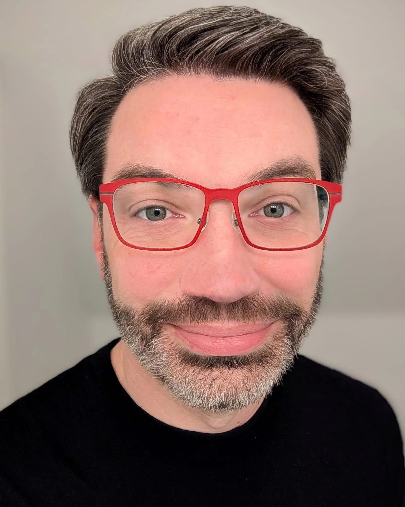 Headshot of John with warm smile wearing a back sweater and red rimmed glasses