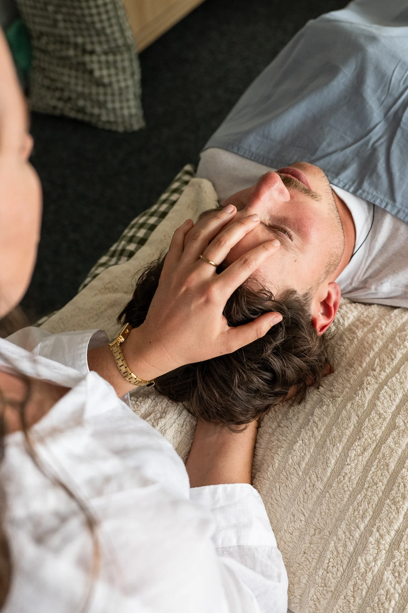 Client laying on a treatment table, with an Osteopath gently touching a man's face and back of head.