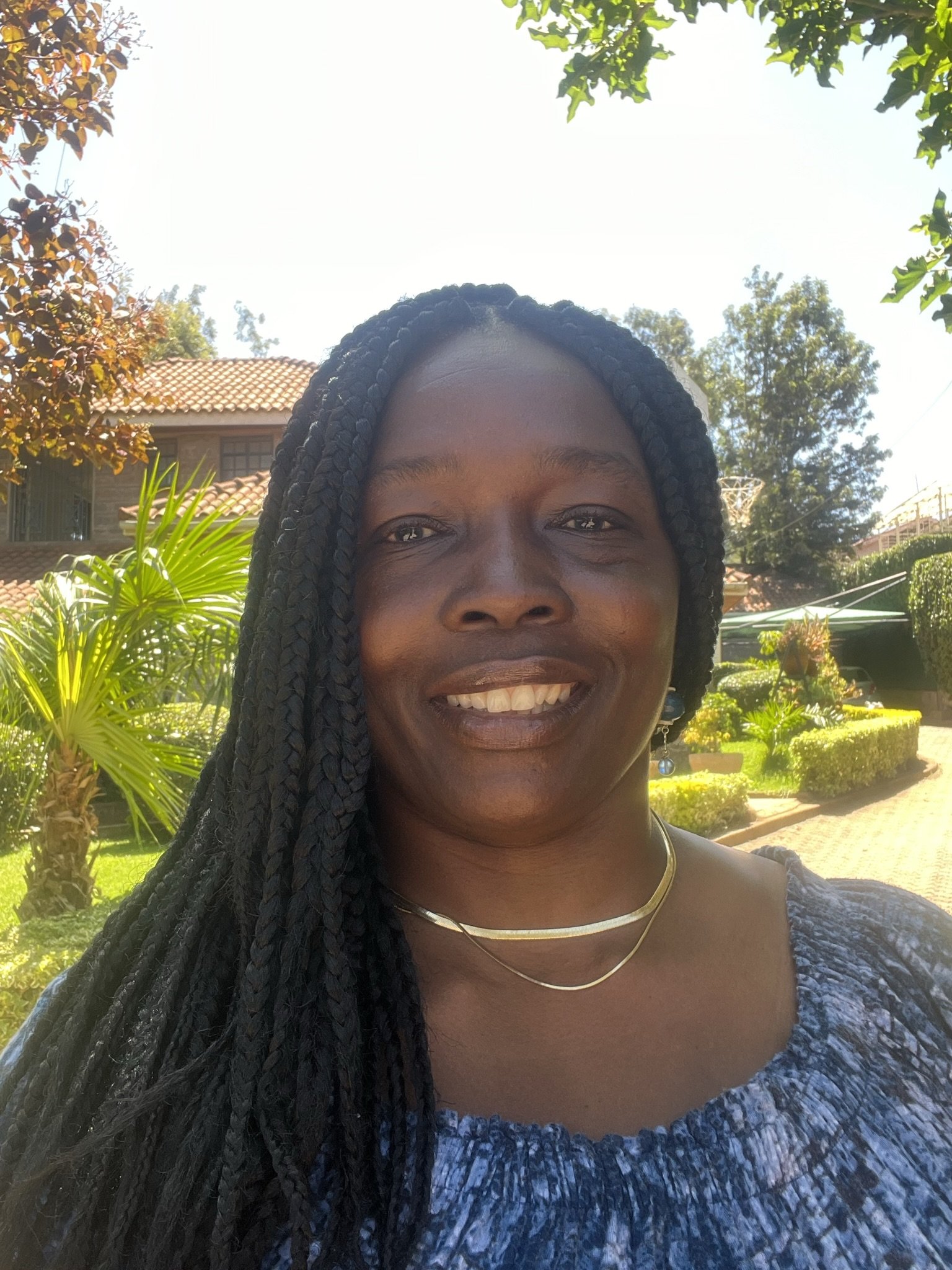 A woman with braided hair smiling outdoors with garden and house in the background