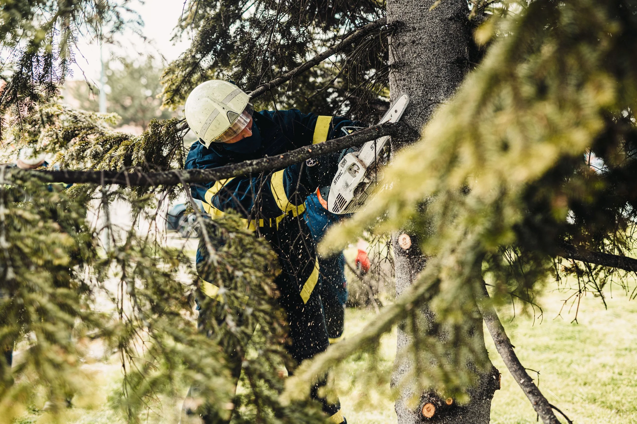 A firefighter cutting a fallen tree with a chainsaw during a storm or cleanup.