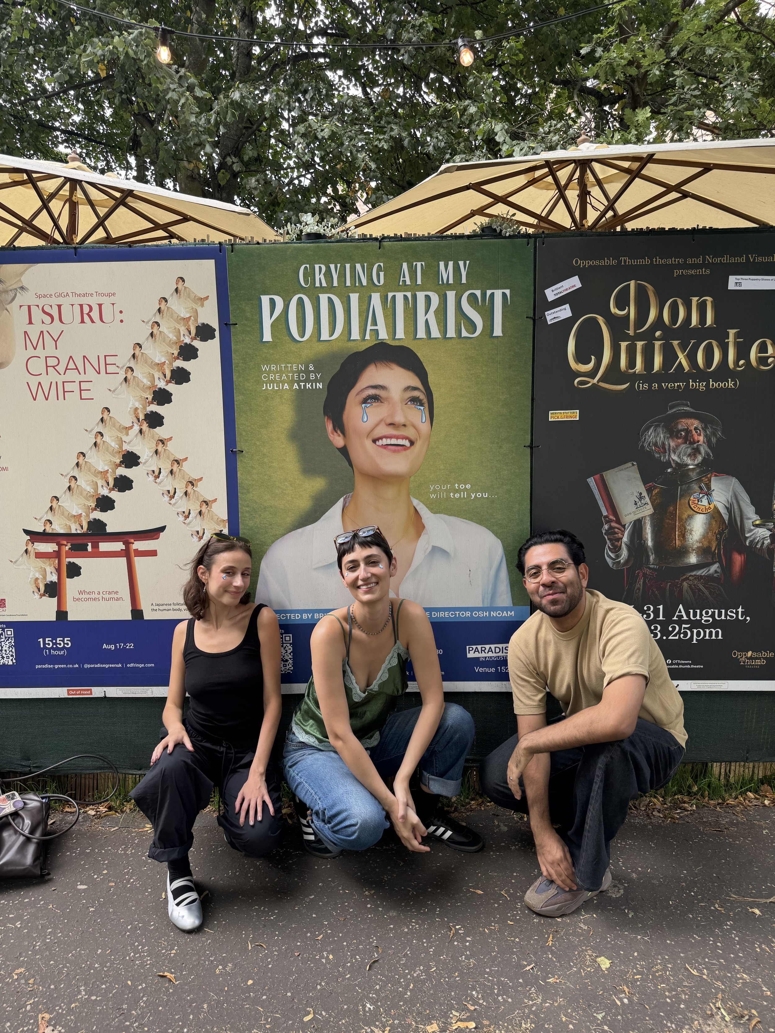 Julia Atkin, Britt Berke, and Osh Noam sitting in front of the poster for Crying at My Podiatrist