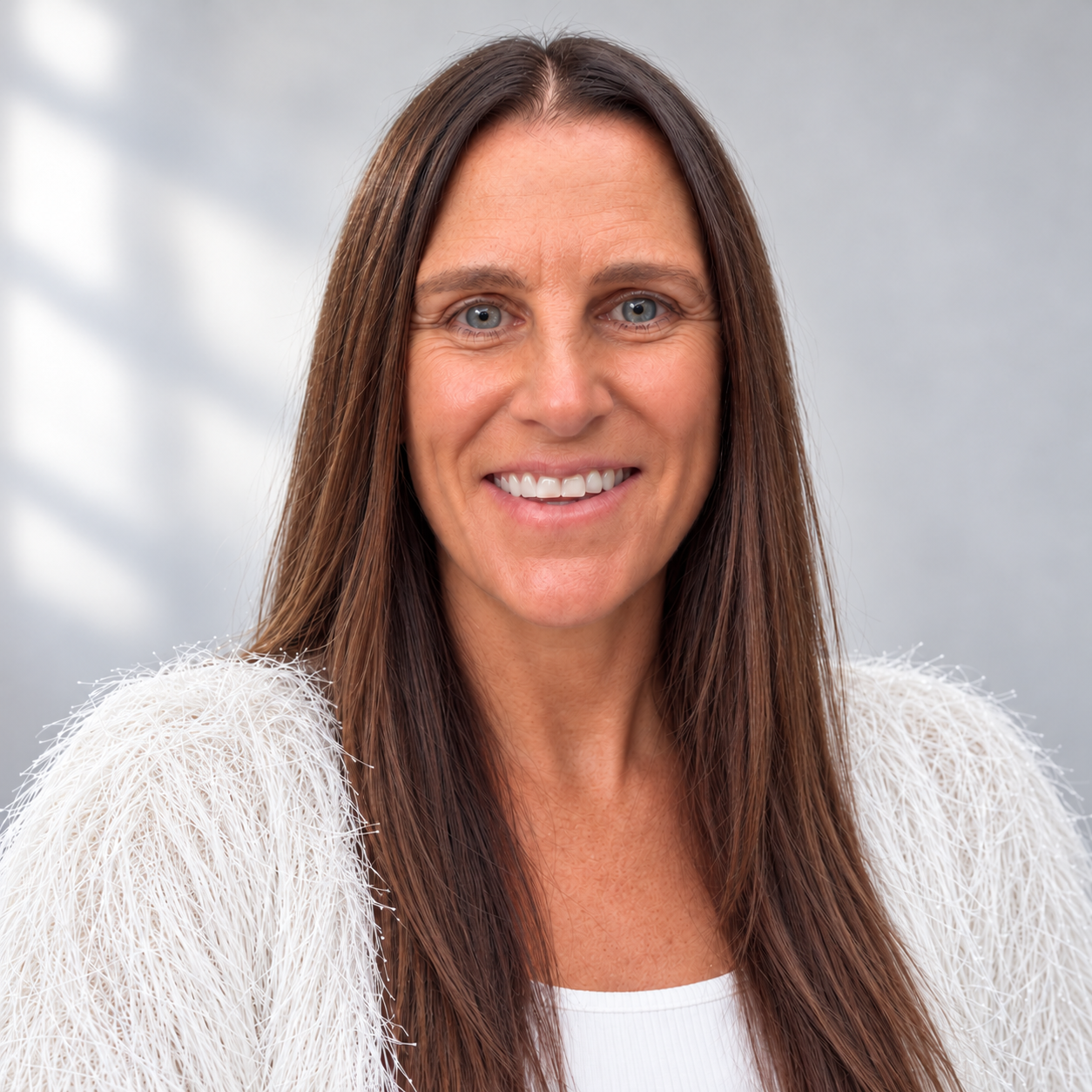 Smiling portrait of Justine with long brown hair wearing a white textured sweater against a light grey background