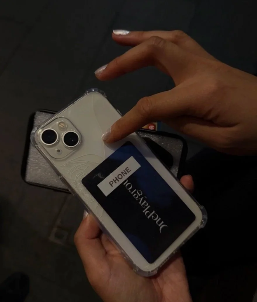 Person holding a white iPhone with a clear case, showing a black card labeled 'Digital Shopping' and a smaller sticker labeled 'Phone'.
