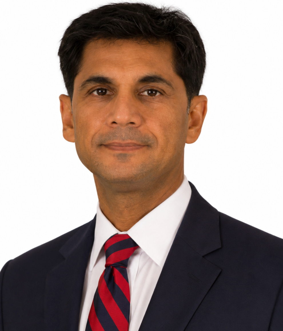 A man with short dark hair wearing a dark suit, white shirt, and a red and blue striped tie, posing against a white background.