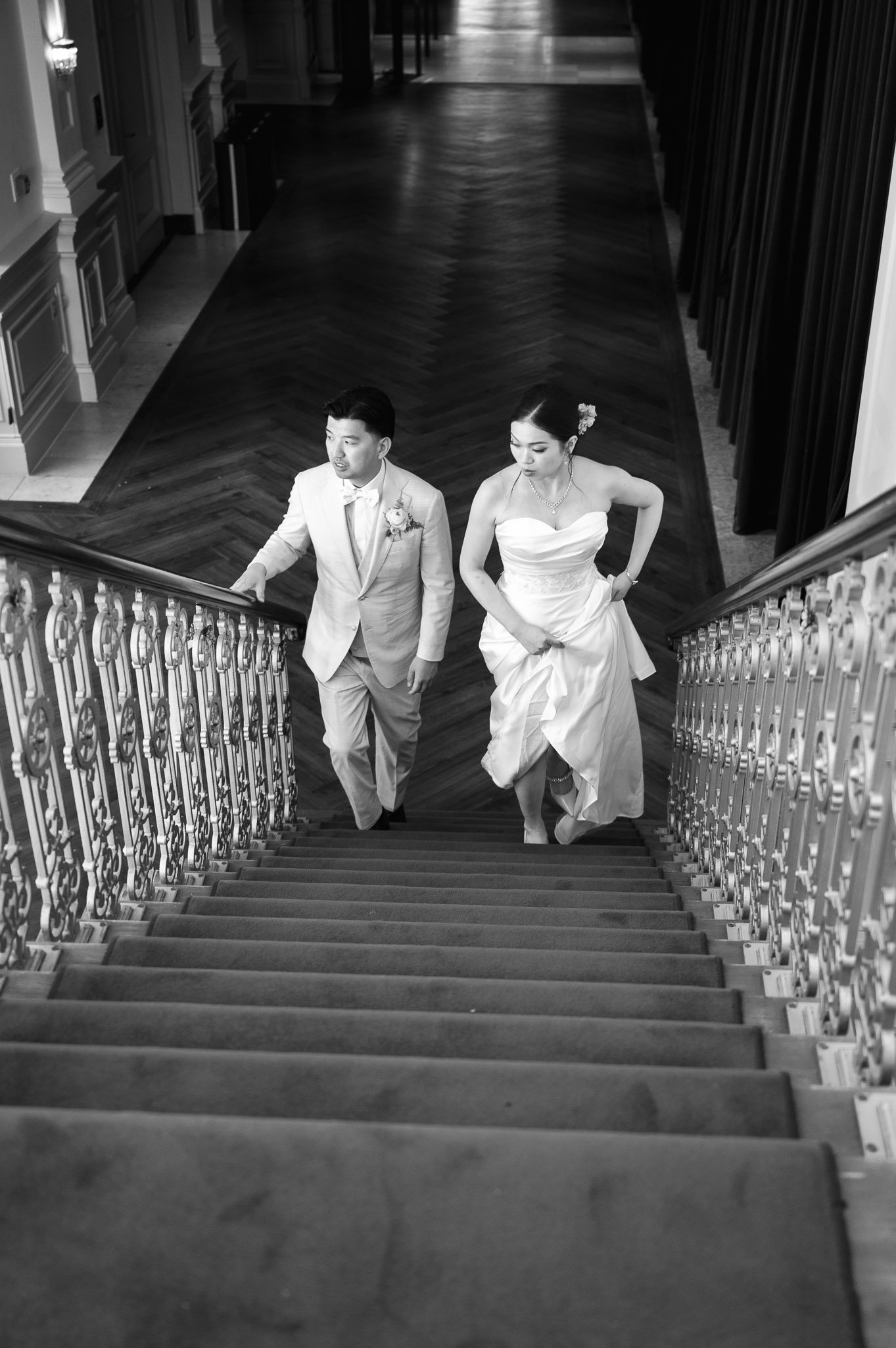 Black-and-white wedding portrait of a bride and groom climbing an ornate staircase.