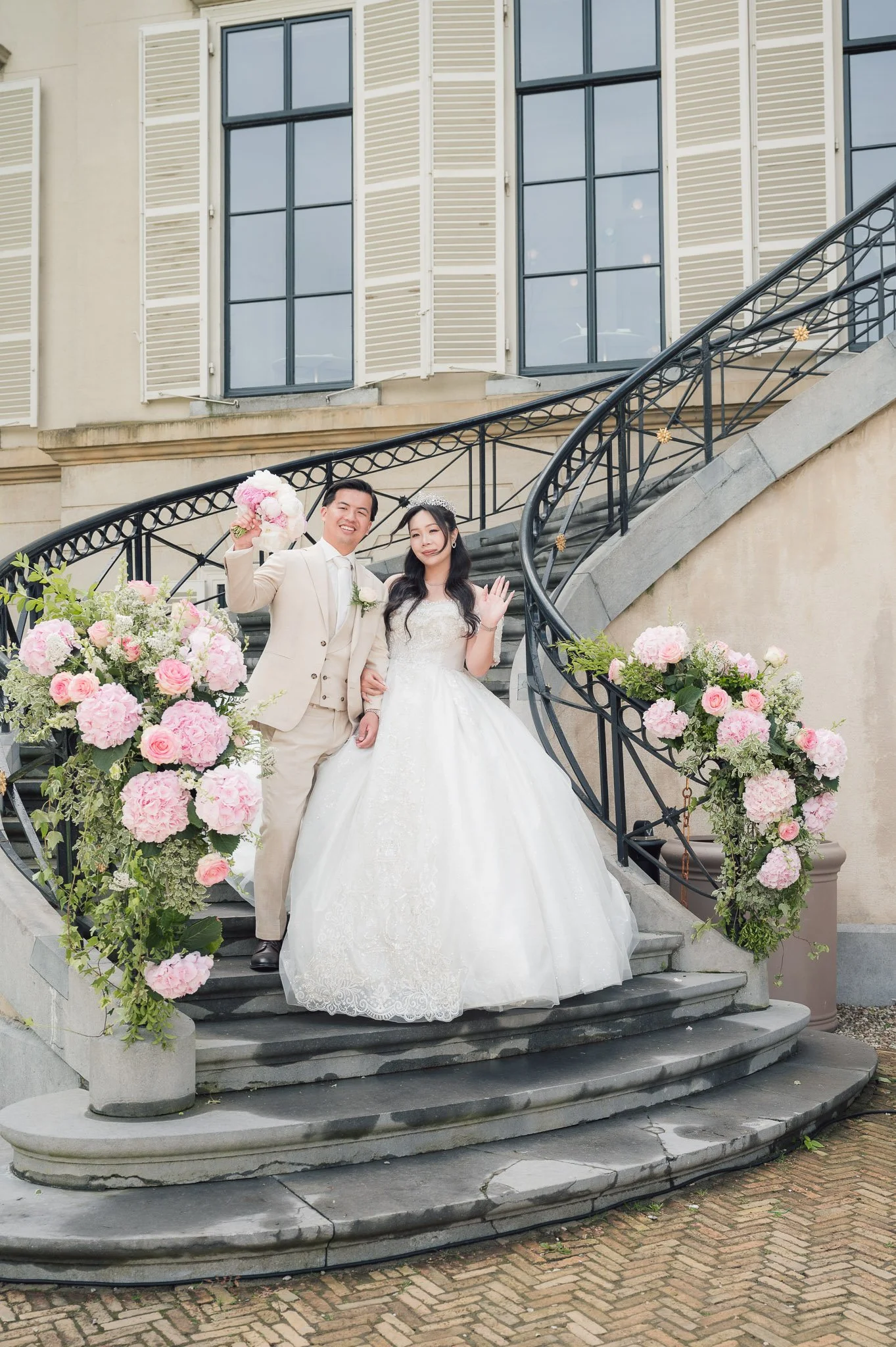 Bride and groom posing on a decorated staircase surrounded by pink and white wedding flowers