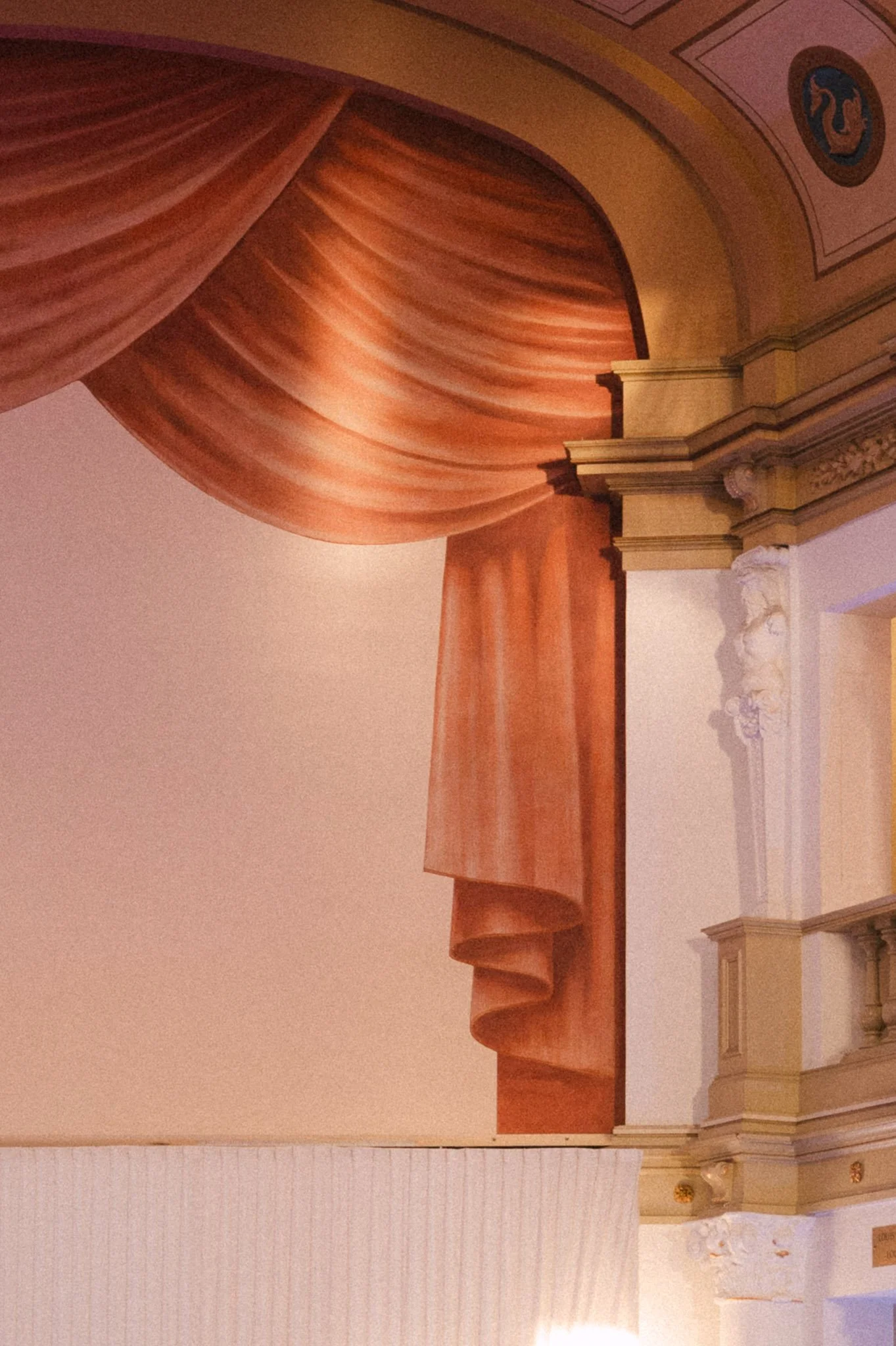Ornate theater interior with red velvet stage curtains, classical columns, and decorative ceiling details