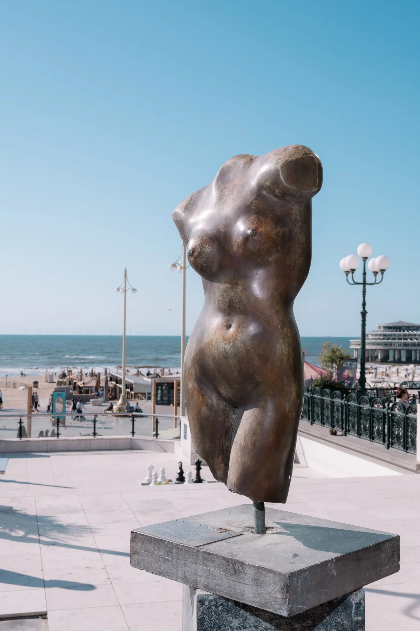 Bronze abstract torso sculpture on a seaside promenade overlooking the beach and ocean