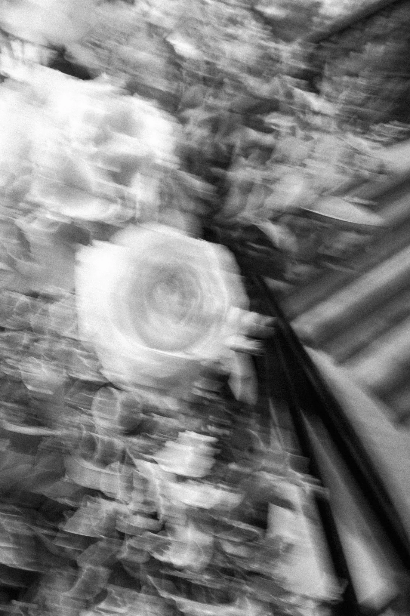 Blurry black-and-white motion photograph of a person riding a bicycle outdoors.