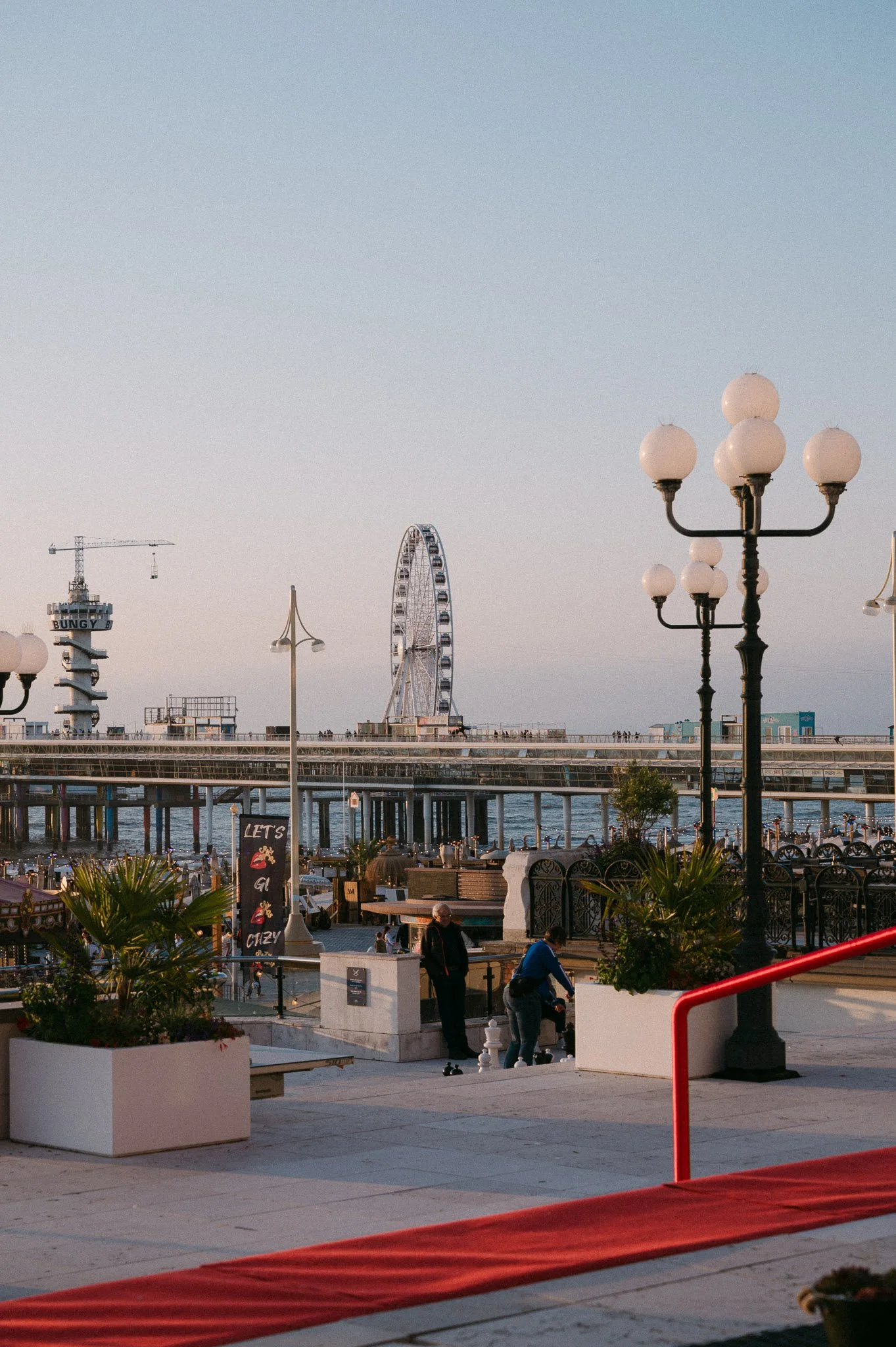 Brighton Palace Pier with a Ferris wheel, amusement rides, ornate globe streetlamps, and a red carpet overlooking the seafront