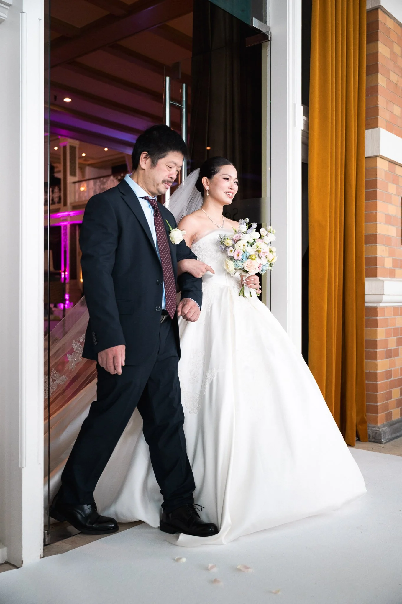Bride carrying a bouquet walks arm-in-arm with a groom through a wedding venue doorway.