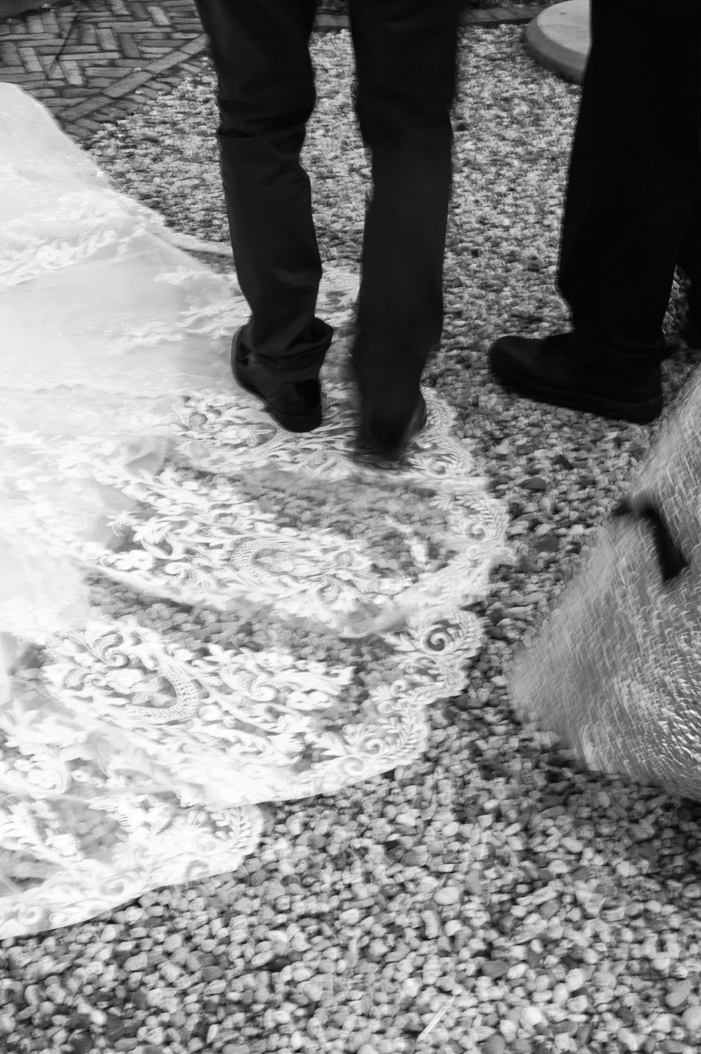 Black-and-white photo of several people standing on a floral-patterned rug over a pebble-covered floor.