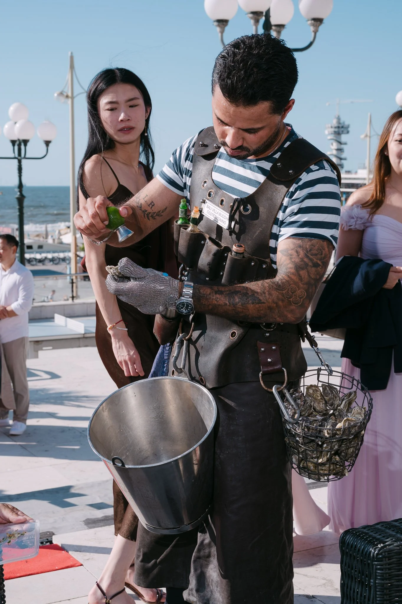 Bartender shucking oysters and squeezing lime at a seaside outdoor event.