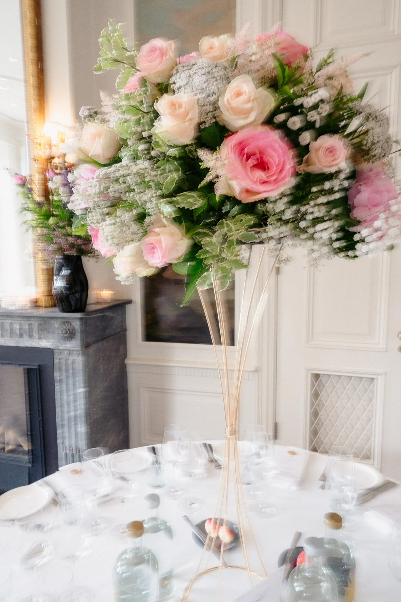 Elegant dining table with a tall pink and peach rose floral centerpiece in a bright formal dining room