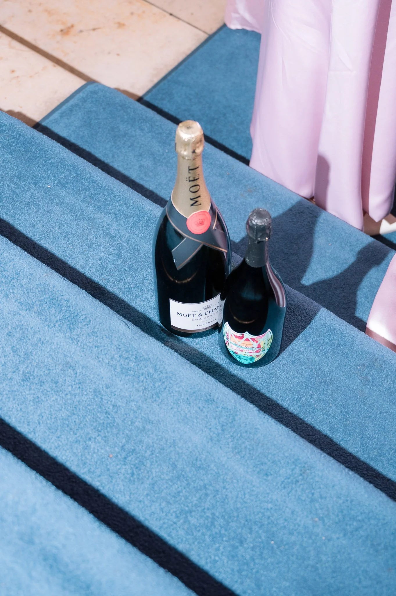 Two champagne bottles, including a Moët & Chandon bottle, on a blue striped tablecloth beside pink drapery.