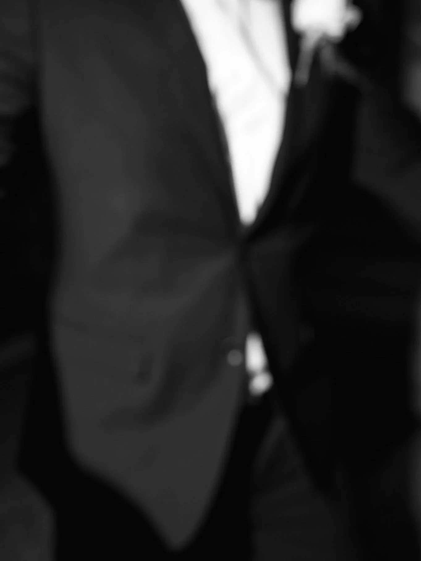 Blurred black-and-white close-up of a person wearing a dark suit and white shirt