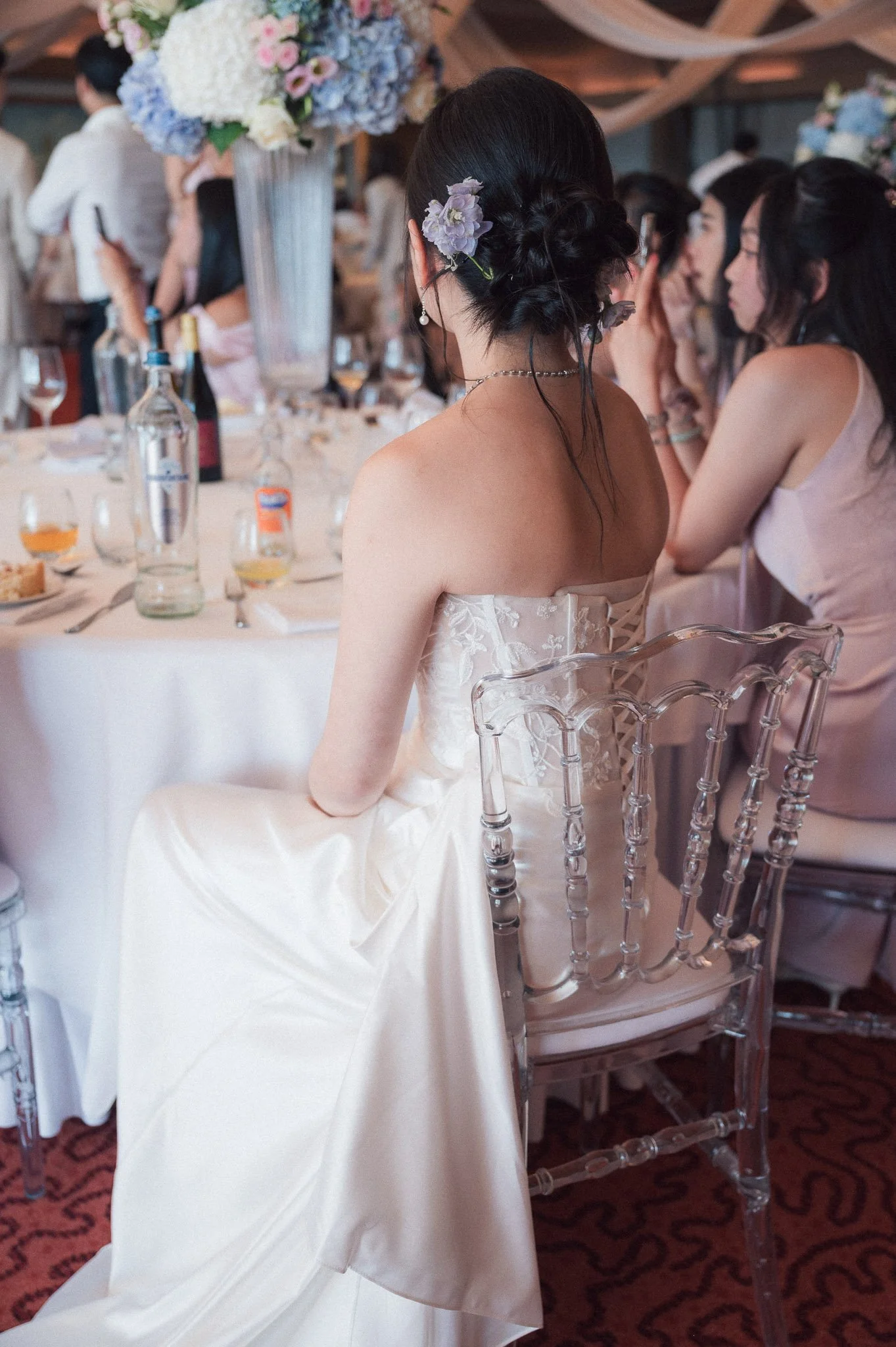 Bride in a white wedding dress with flowers in her hair seated at a decorated wedding reception table.