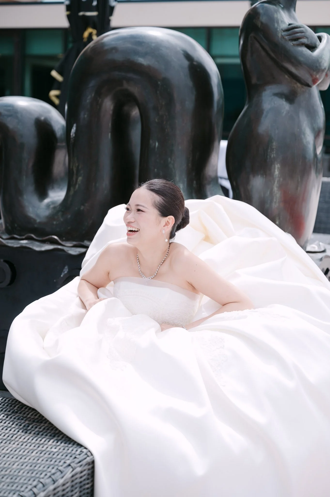 Smiling bride in a strapless white wedding gown posing beside large dark sculptures.