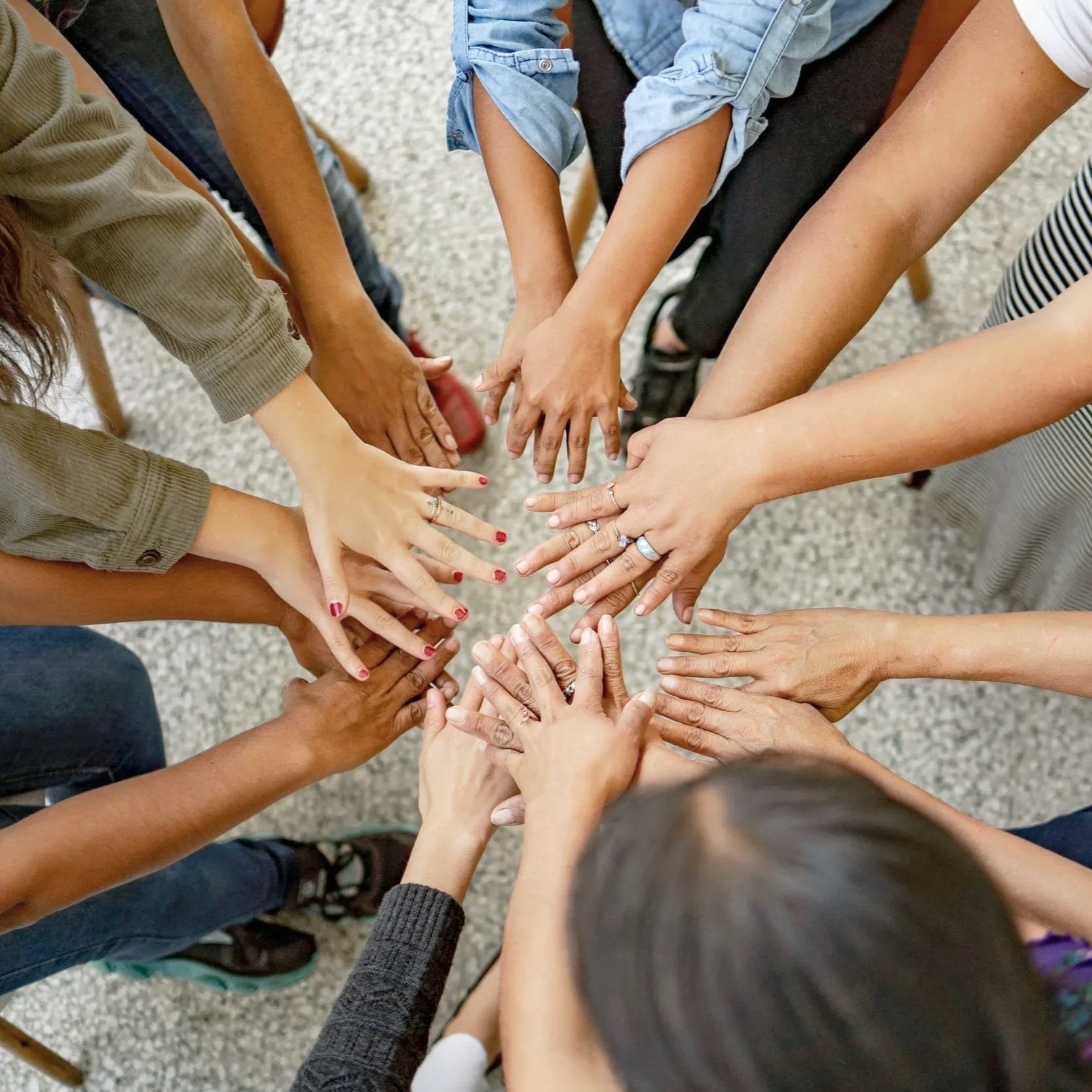 Diverse group of people stacking hands together in a circle during a team-building activity