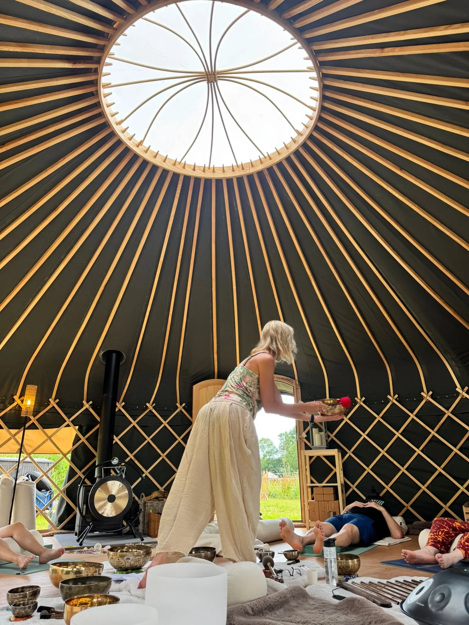 Woman leading a sound bath meditation inside a wooden yurt with singing bowls and reclining participants
