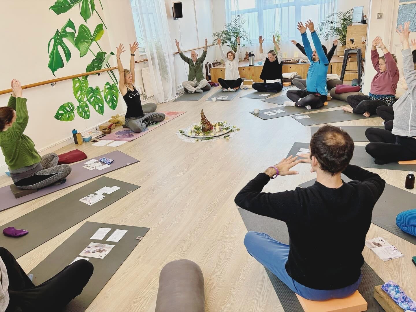 Group yoga class seated on mats with arms raised in a bright studio