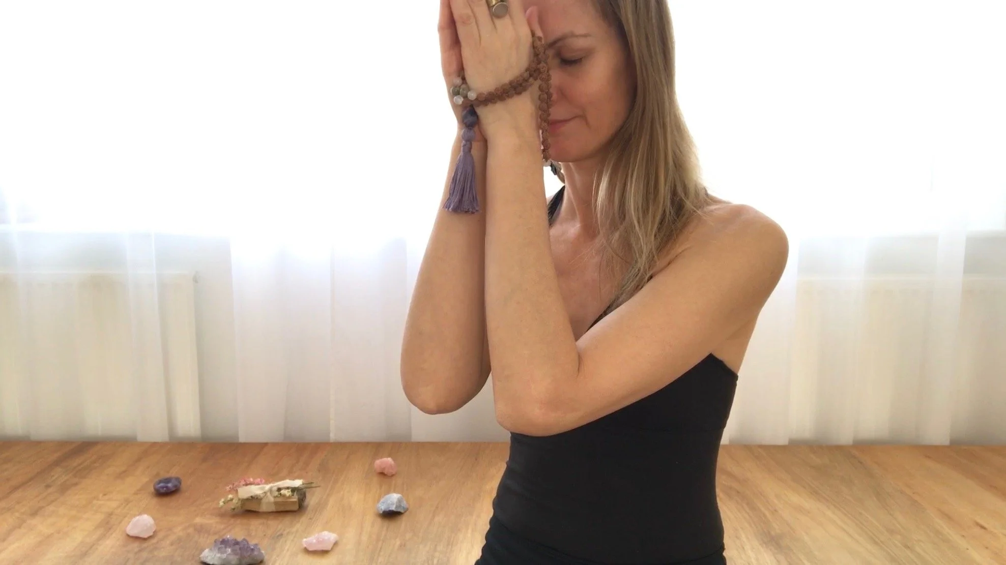 Woman meditating with prayer beads and crystals on a wooden floor