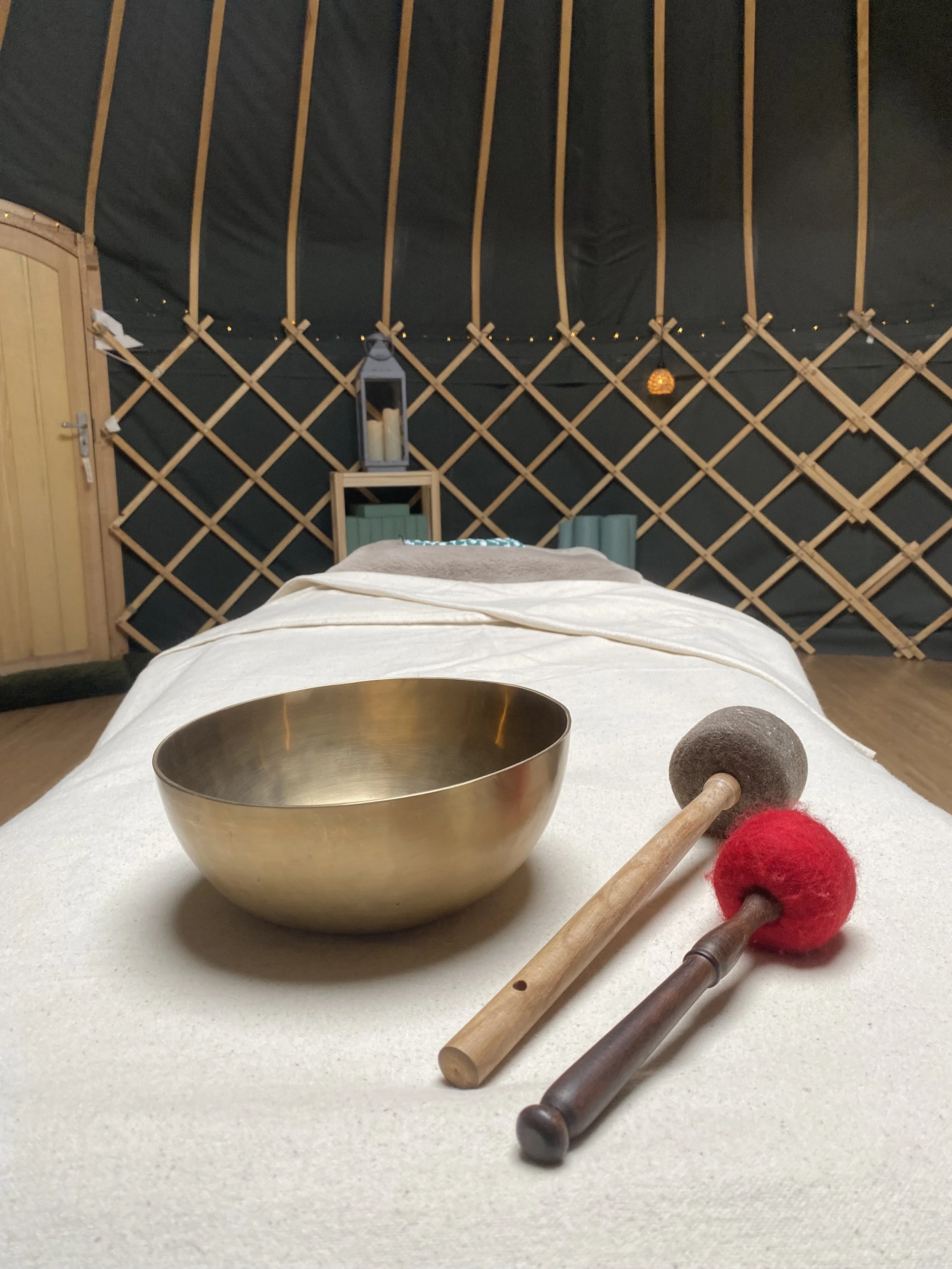 Brass singing bowl with red and black mallets on a massage table in a dimly lit relaxation room