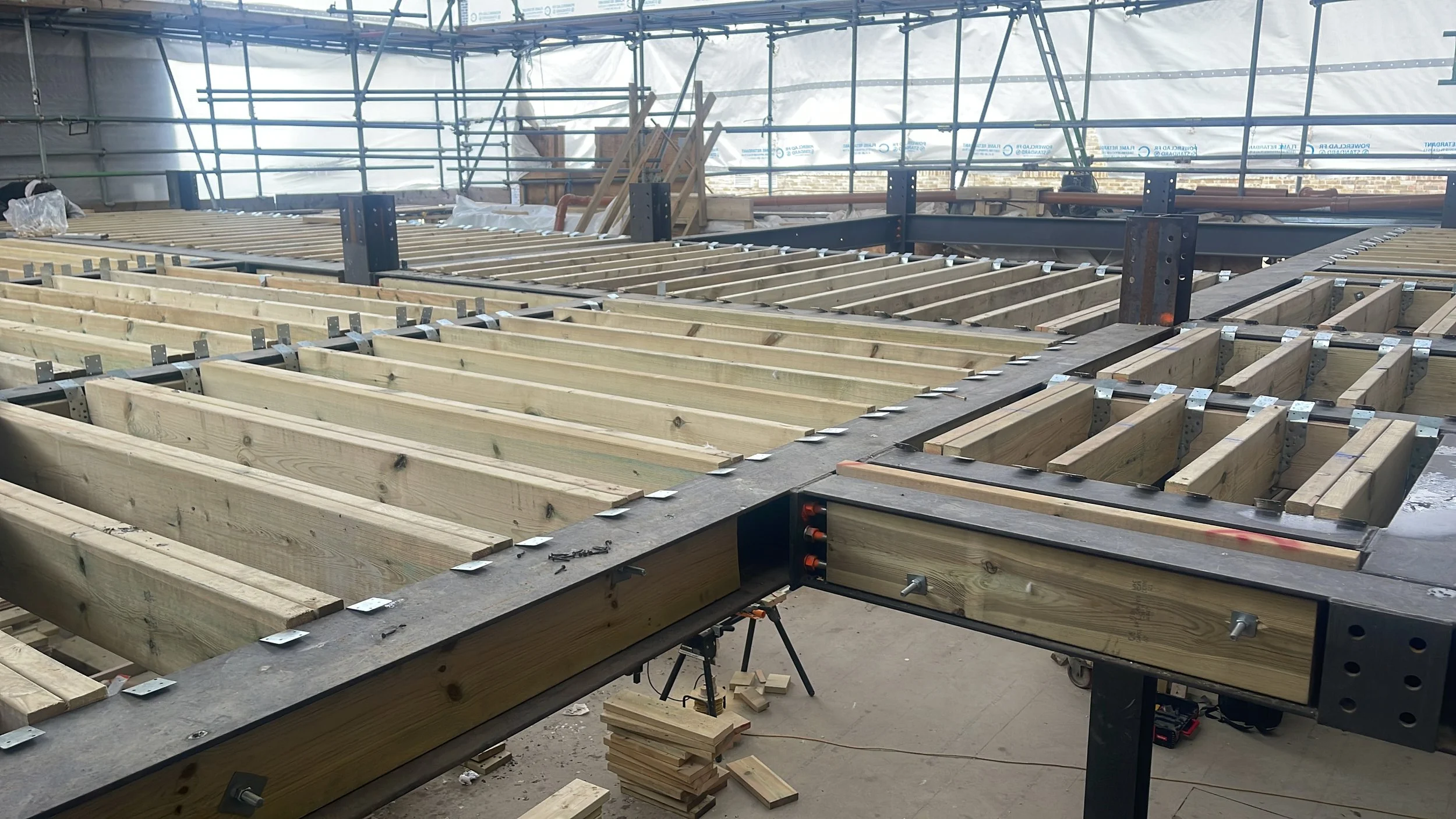 Timber floor joists and steel beams under construction inside a scaffolded building