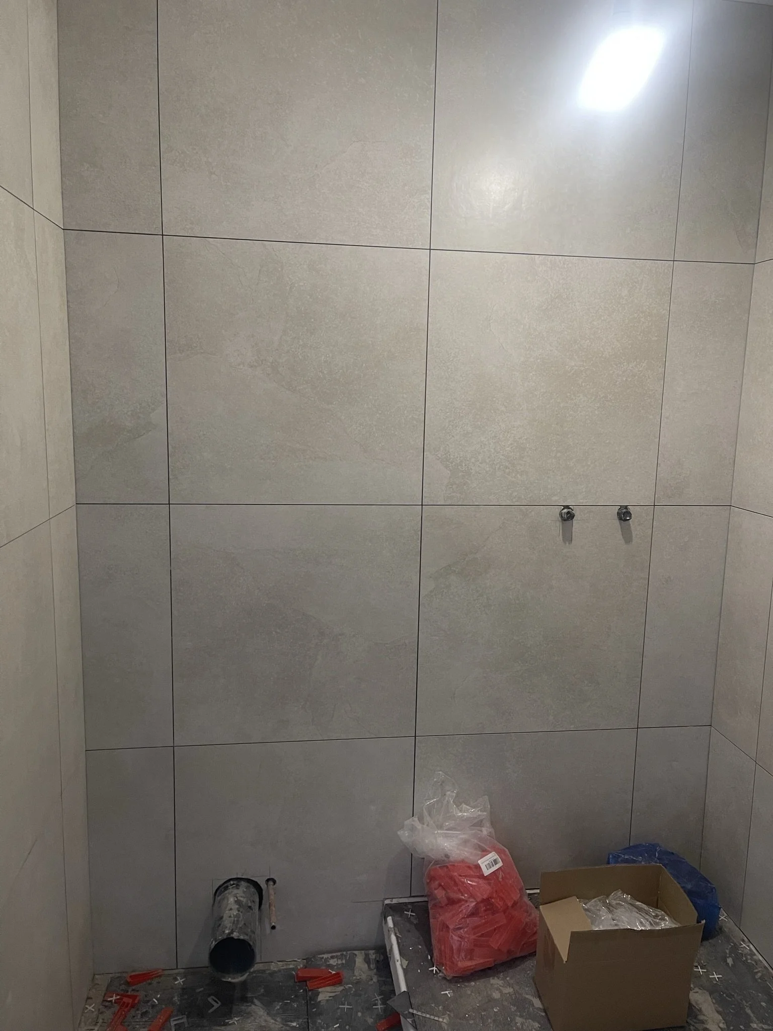 Partially finished bathroom with large gray wall tiles, exposed plumbing, construction materials, and tools on the floor