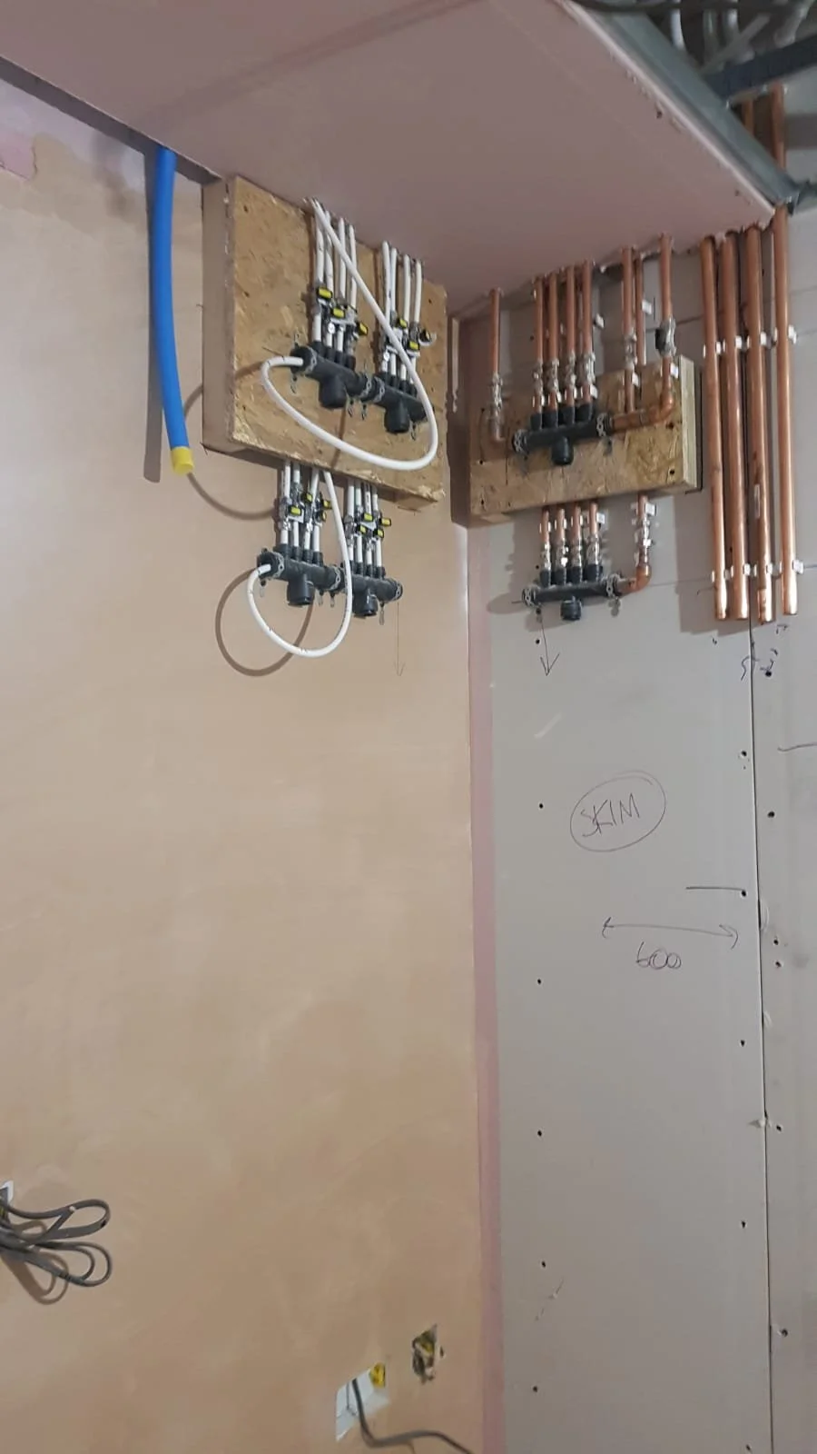 Exposed plumbing manifold with copper and white pipes mounted on plywood panels during building installation