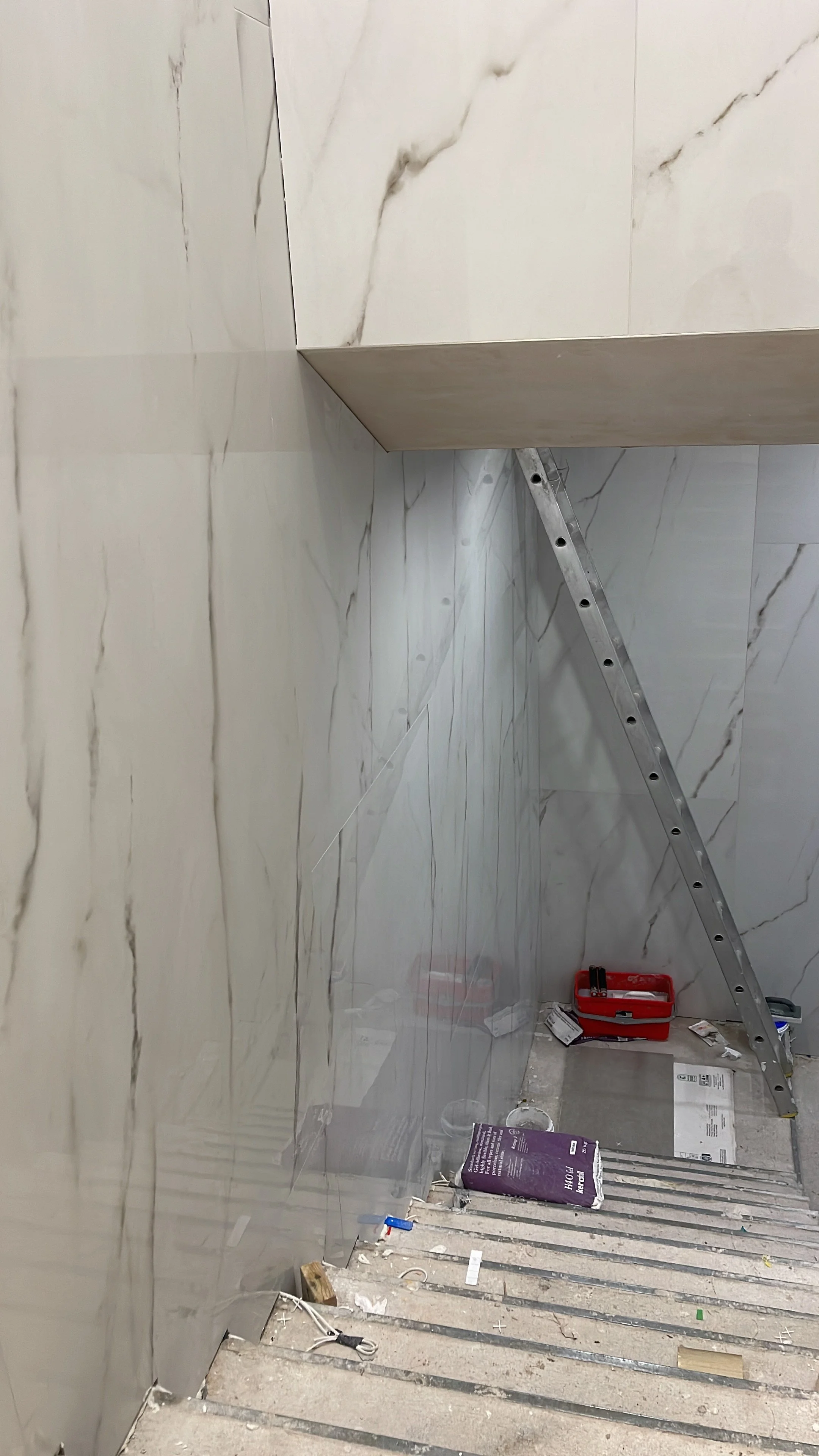 Partially renovated bathroom with marble-look wall tiles, a tiled countertop, ladder, tools, and construction materials.