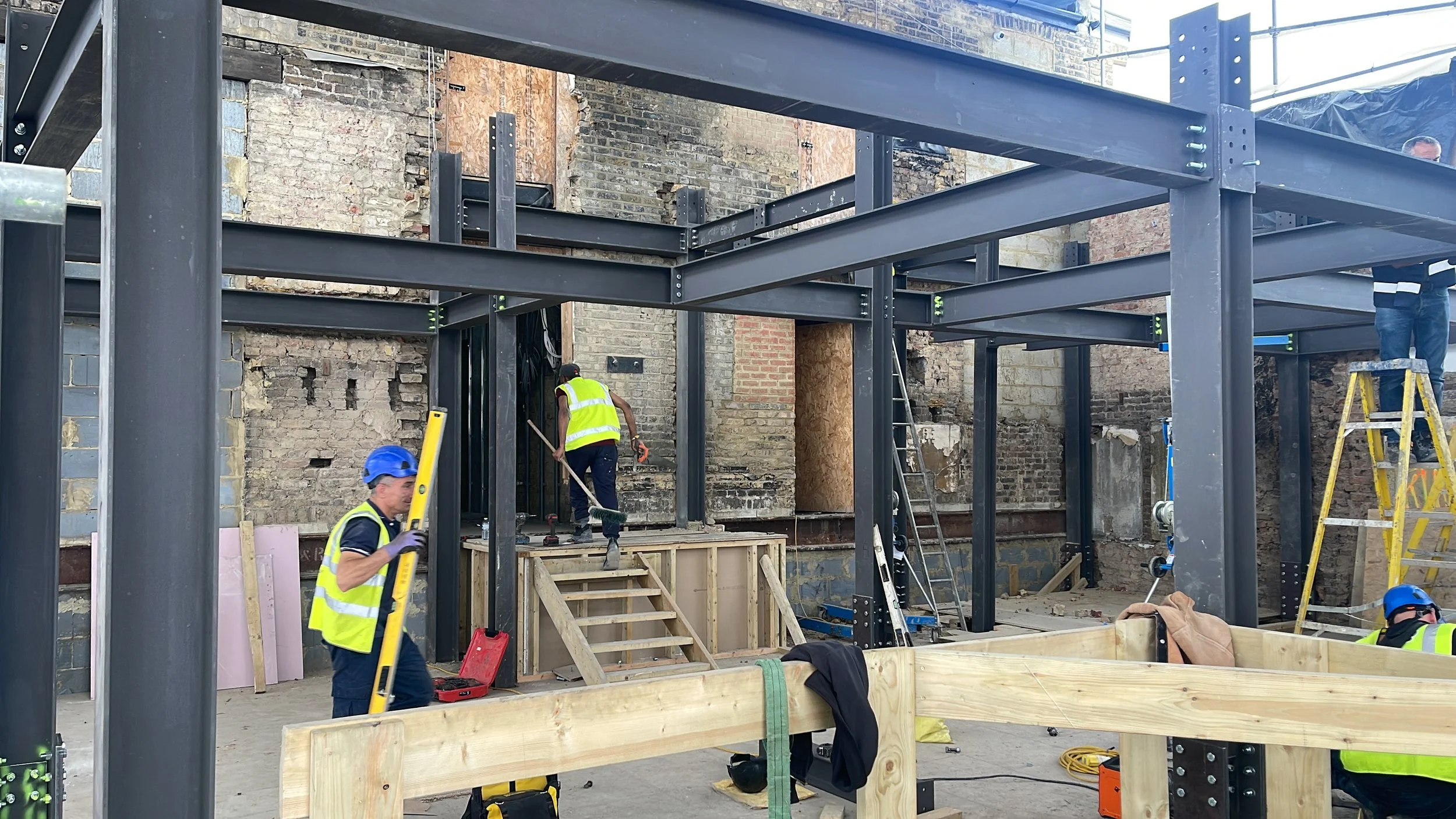 Construction workers assembling a steel frame inside a partially renovated brick building