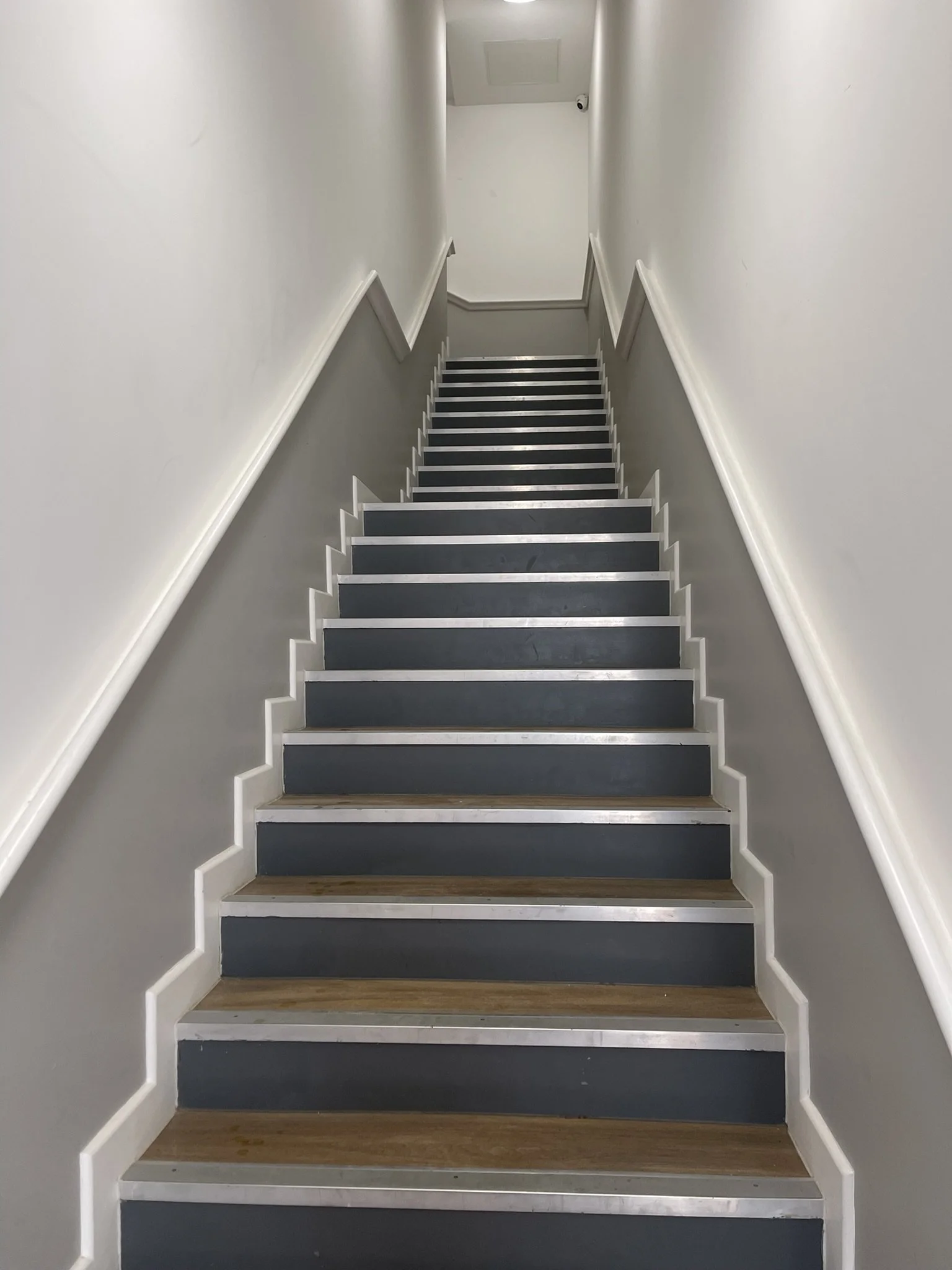 Indoor staircase with dark blue risers, wooden steps, silver metal edges, and white handrails