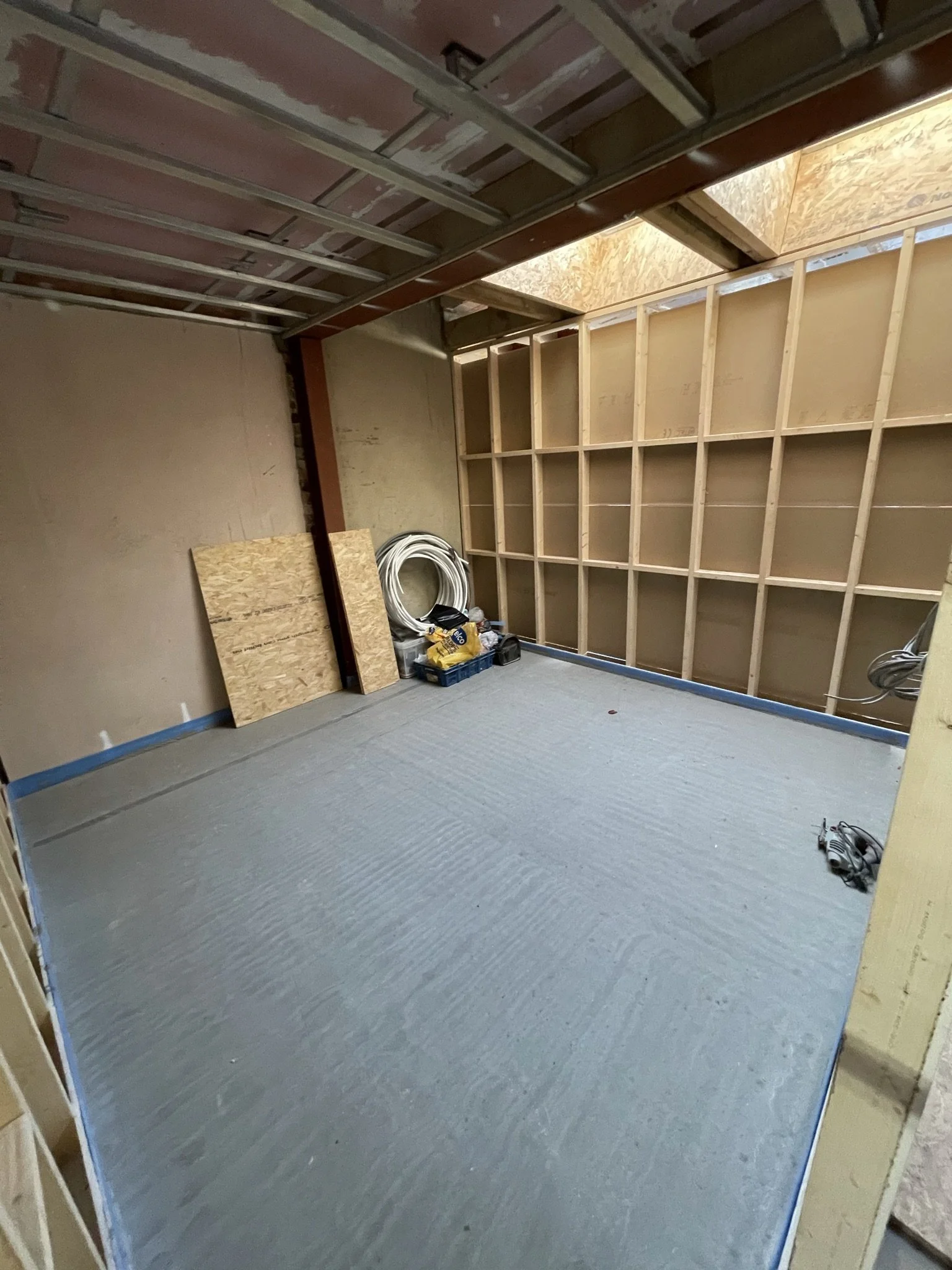 Unfinished basement room under renovation with exposed wall framing, partially installed drywall ceiling, construction materials, and coiled cable.