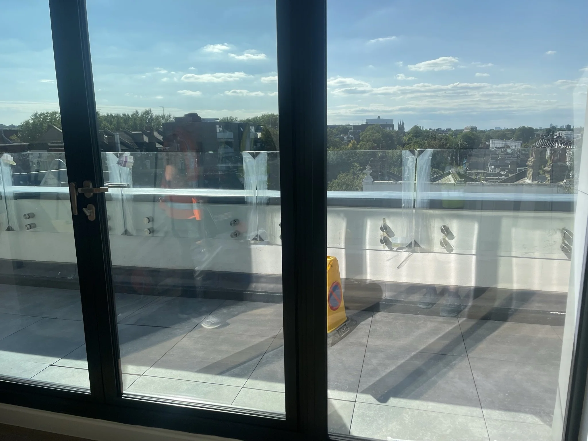 View of London rooftops and trees through glass balcony doors on a sunny day