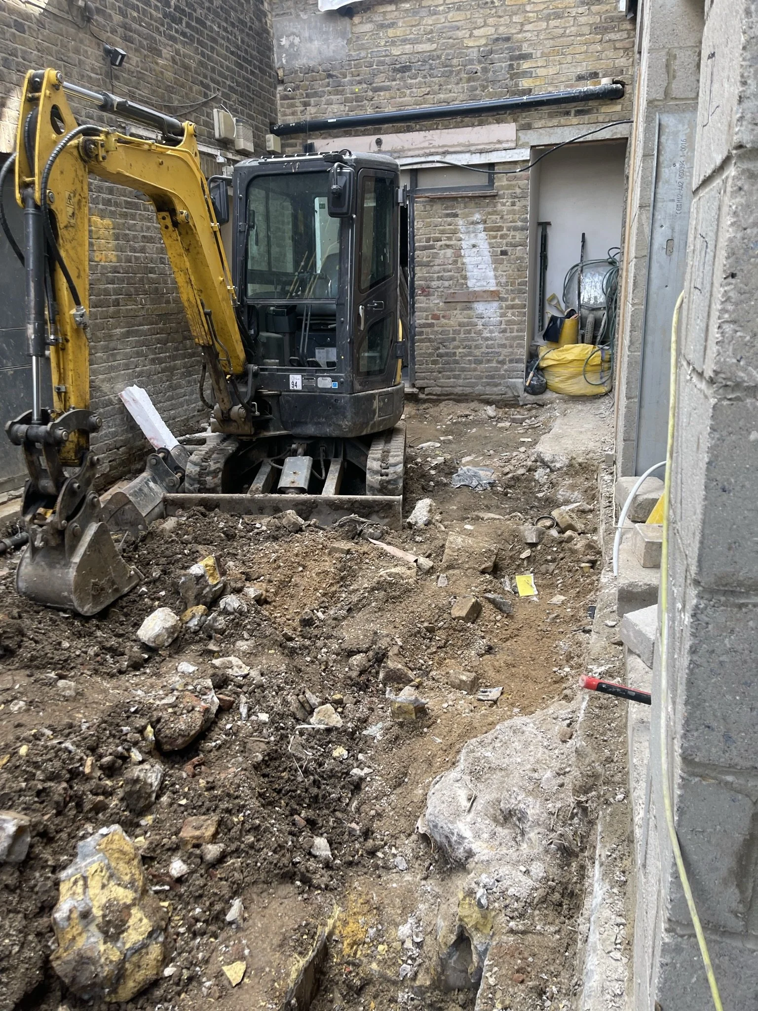 Compact excavator digging rubble in a narrow brick-walled construction site
