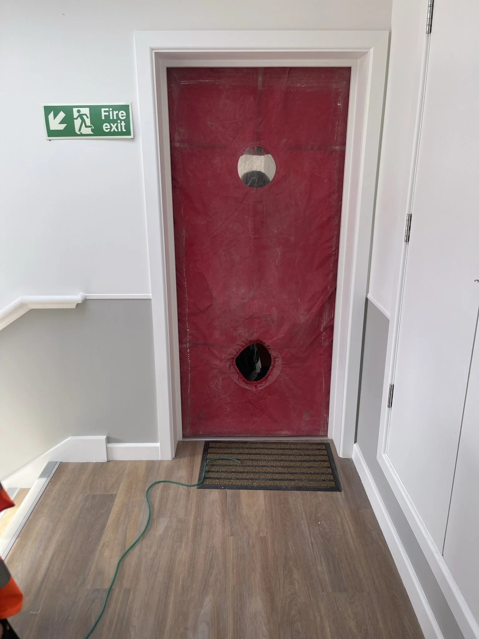 Red-covered door beneath a green fire exit sign in an indoor hallway