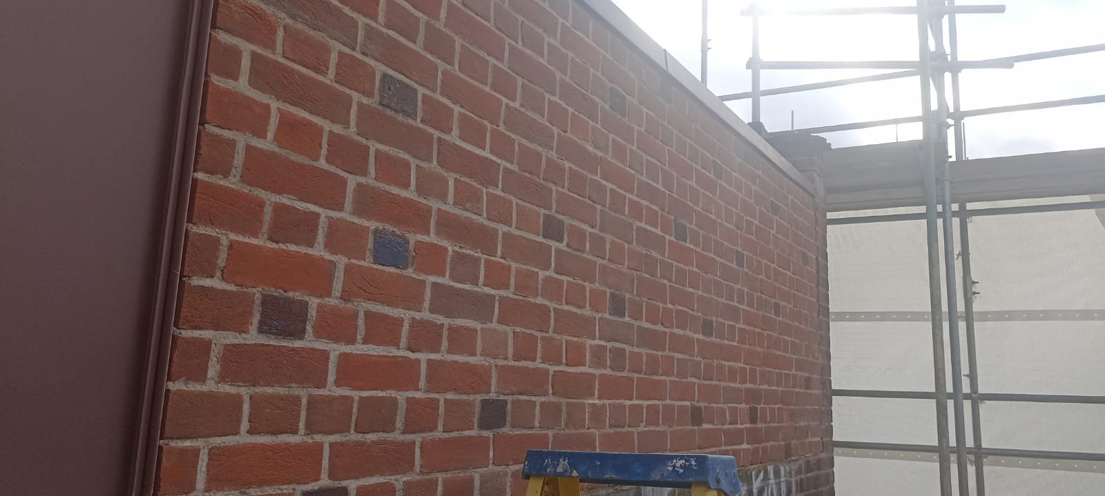 Red brick wall under construction with scaffolding and a blue-topped step ladder