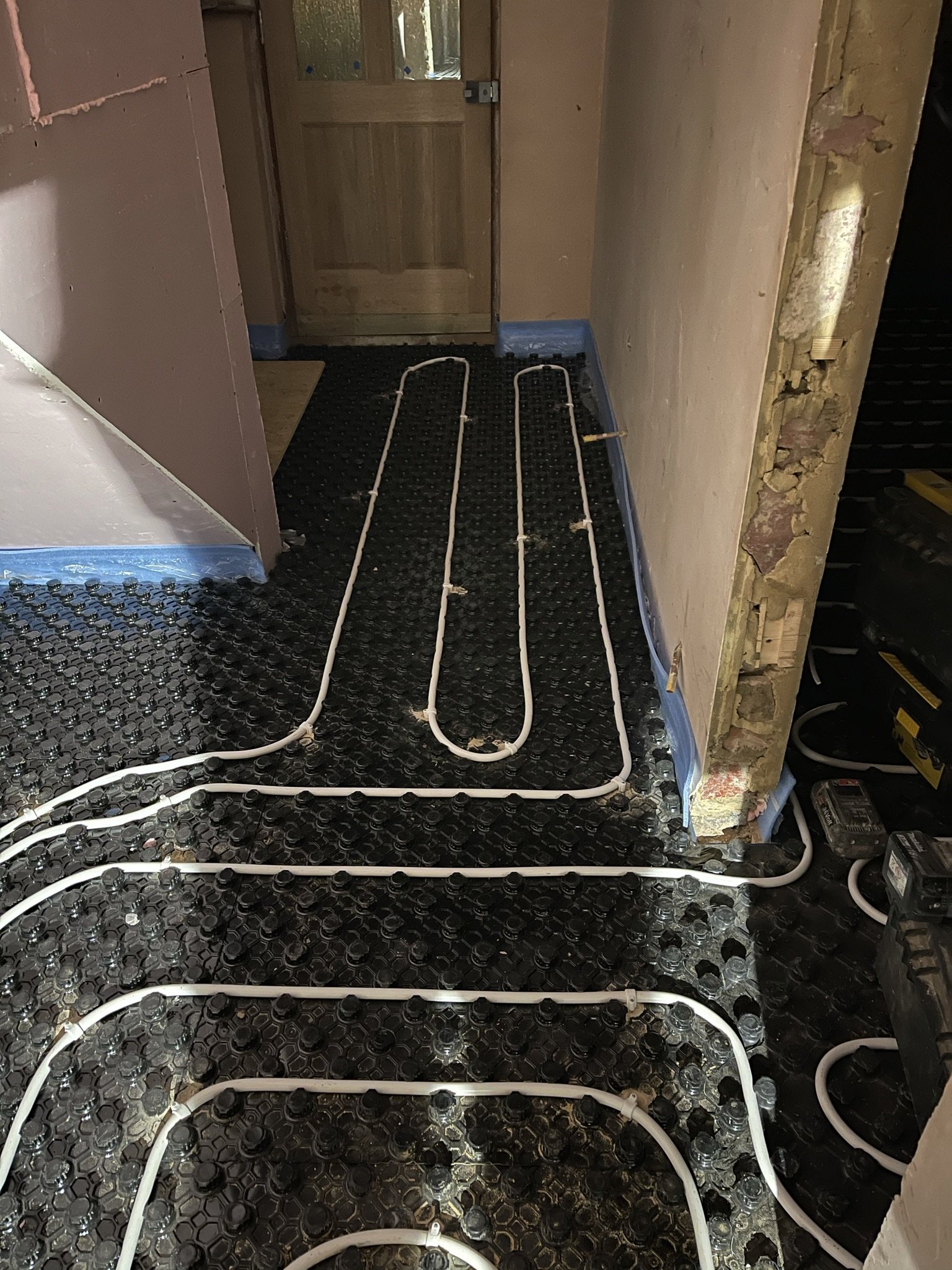 White underfloor heating pipes installed in loops over black insulation panels during floor renovation