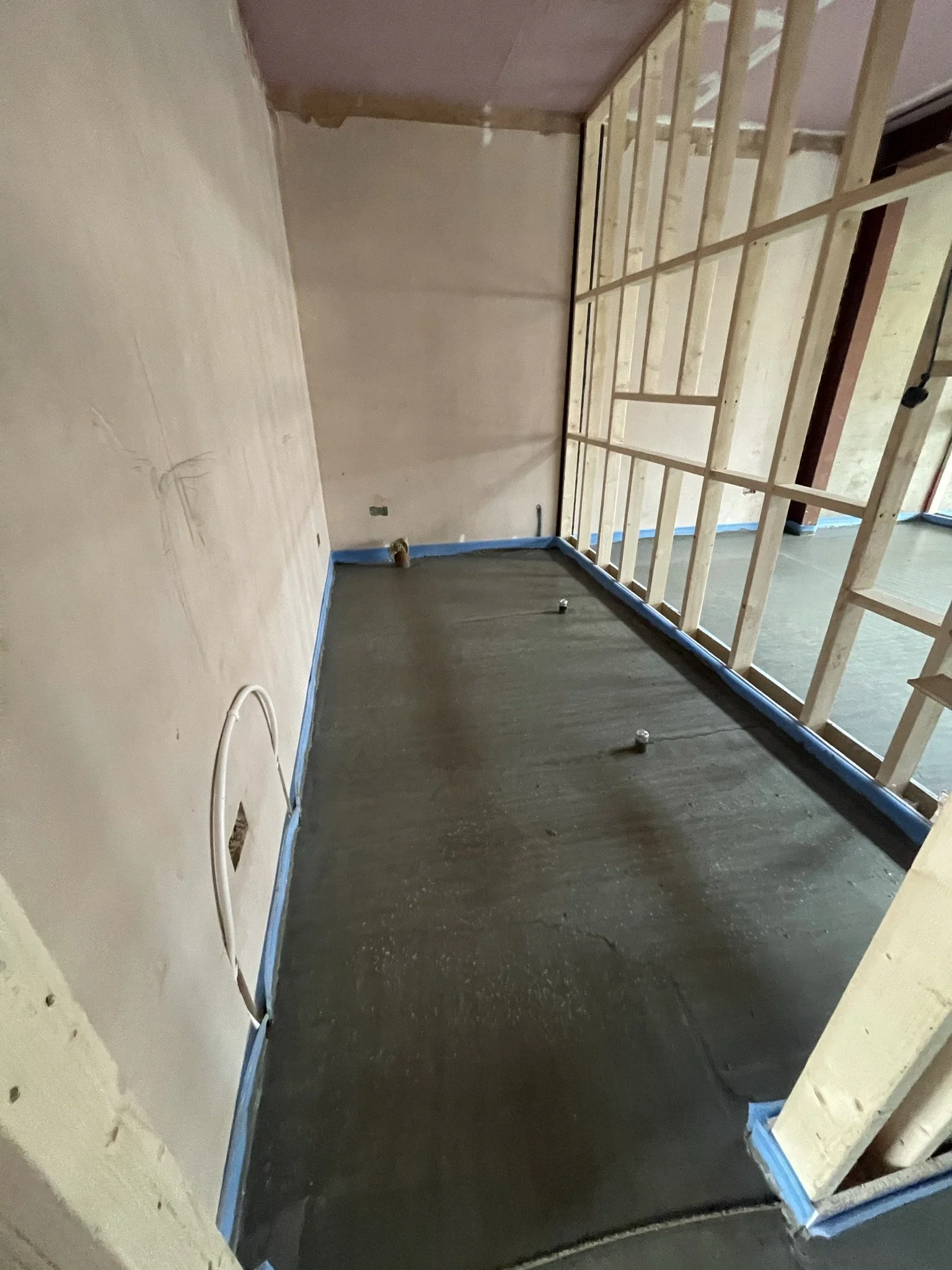 Renovation area with freshly poured dark concrete floor, blue painter’s tape along the edges, and exposed wood framing.
