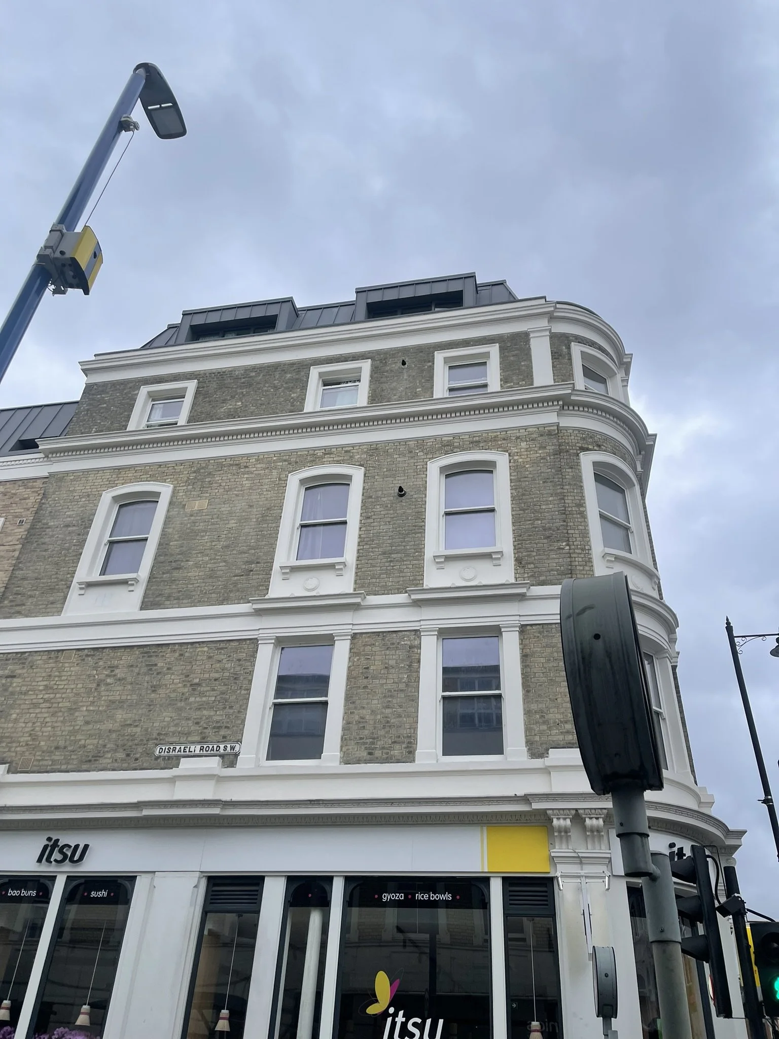 Historic brick corner building housing an Itsu restaurant on Disraeli Road SW, with ornate white trim and a streetlight overhead