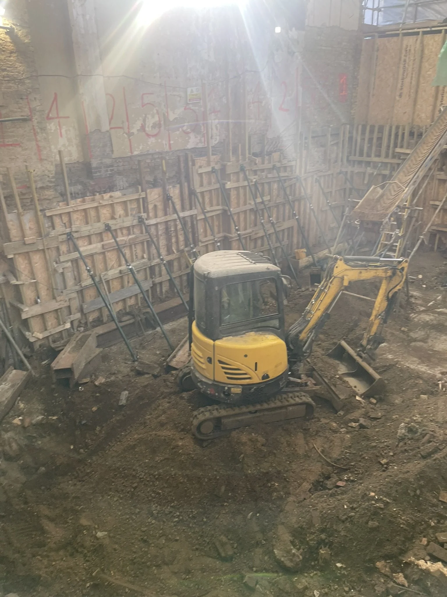 Yellow mini excavator at a construction site with wood shoring and dirt walls
